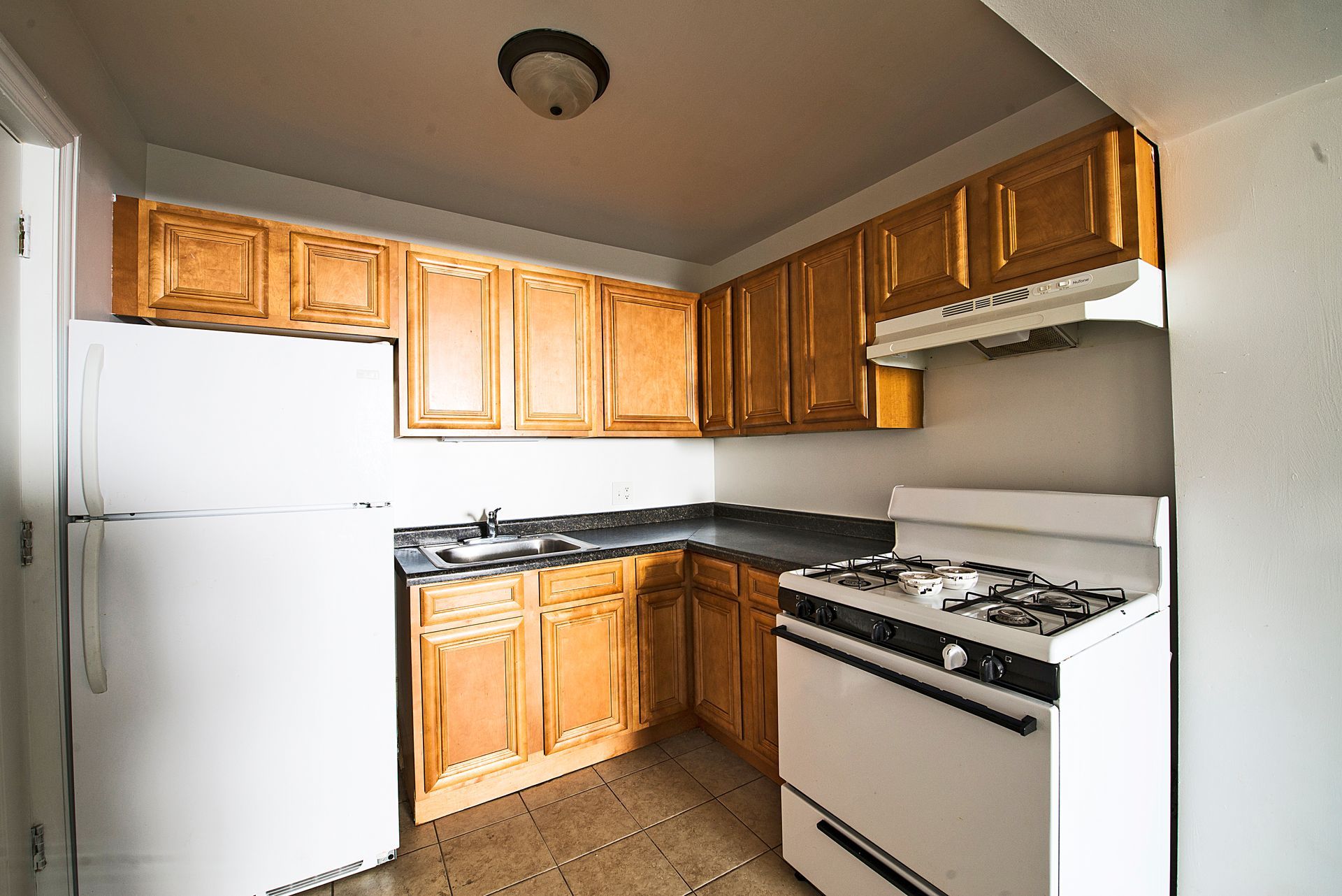 Small kitchen with light wood cabinets, white appliances, and a gas stove.