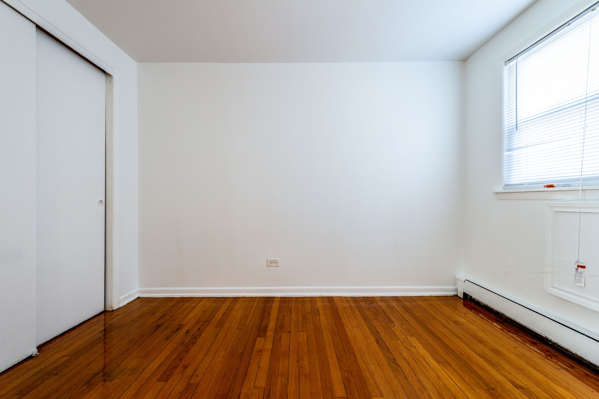 Empty room with hardwood floors, white walls, closet door, and a window with blinds.