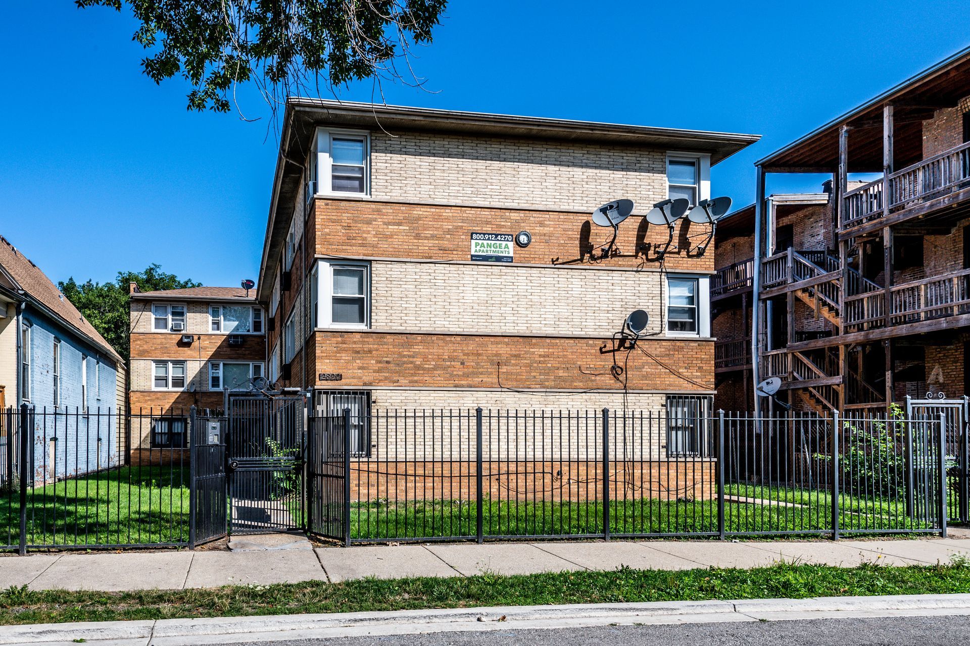 Brick apartment building with a wrought iron fence and satellite dishes on a sunny day.