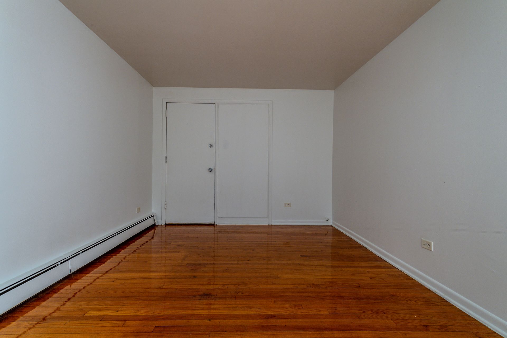 Empty room with white walls, wooden floor, and closet doors.