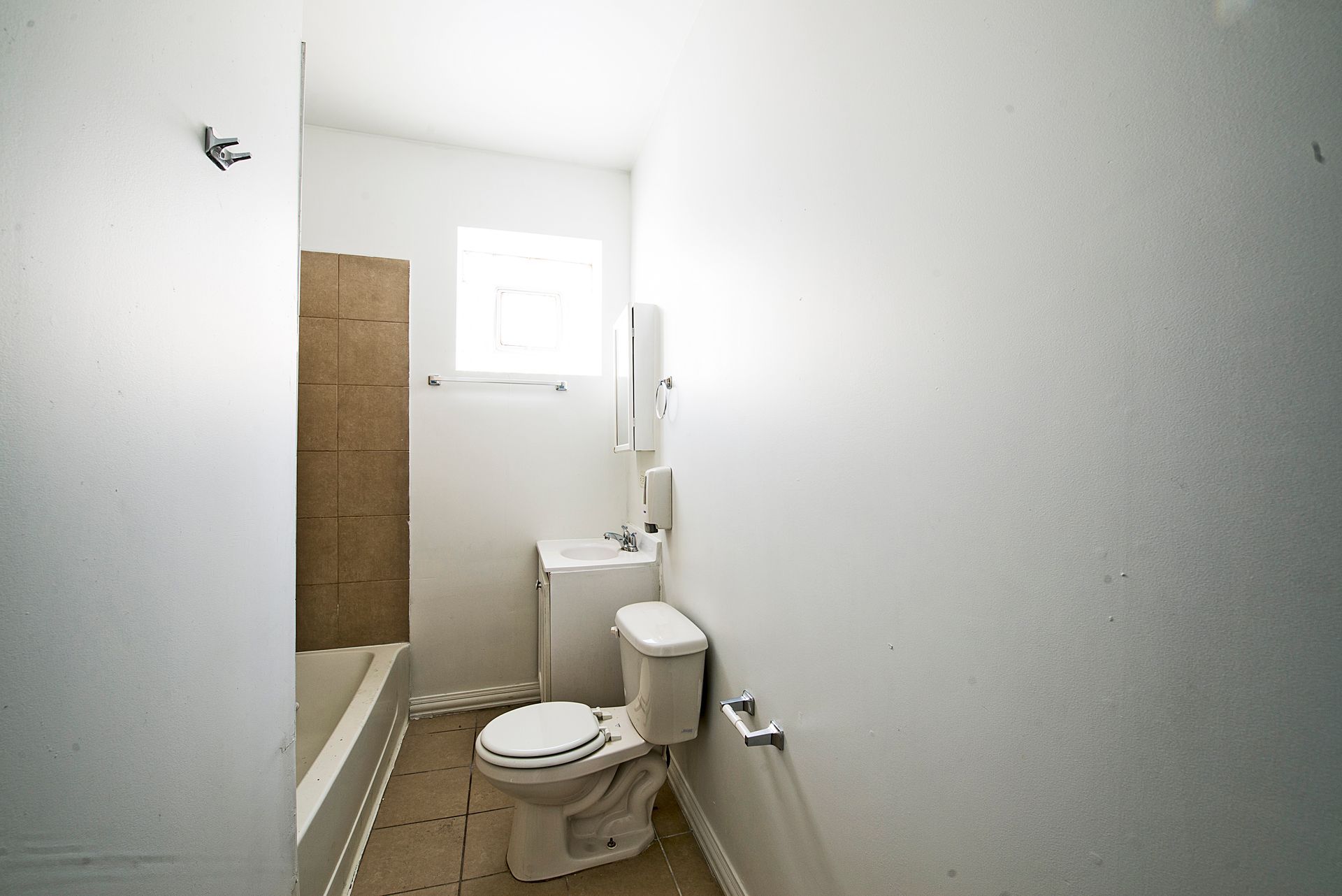 Small, white bathroom with toilet, sink, and tub. A small window provides natural light.