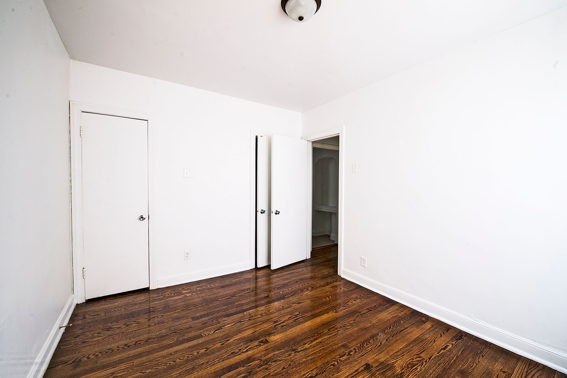 Empty room with hardwood floors, white walls, two closet doors, and a doorway.