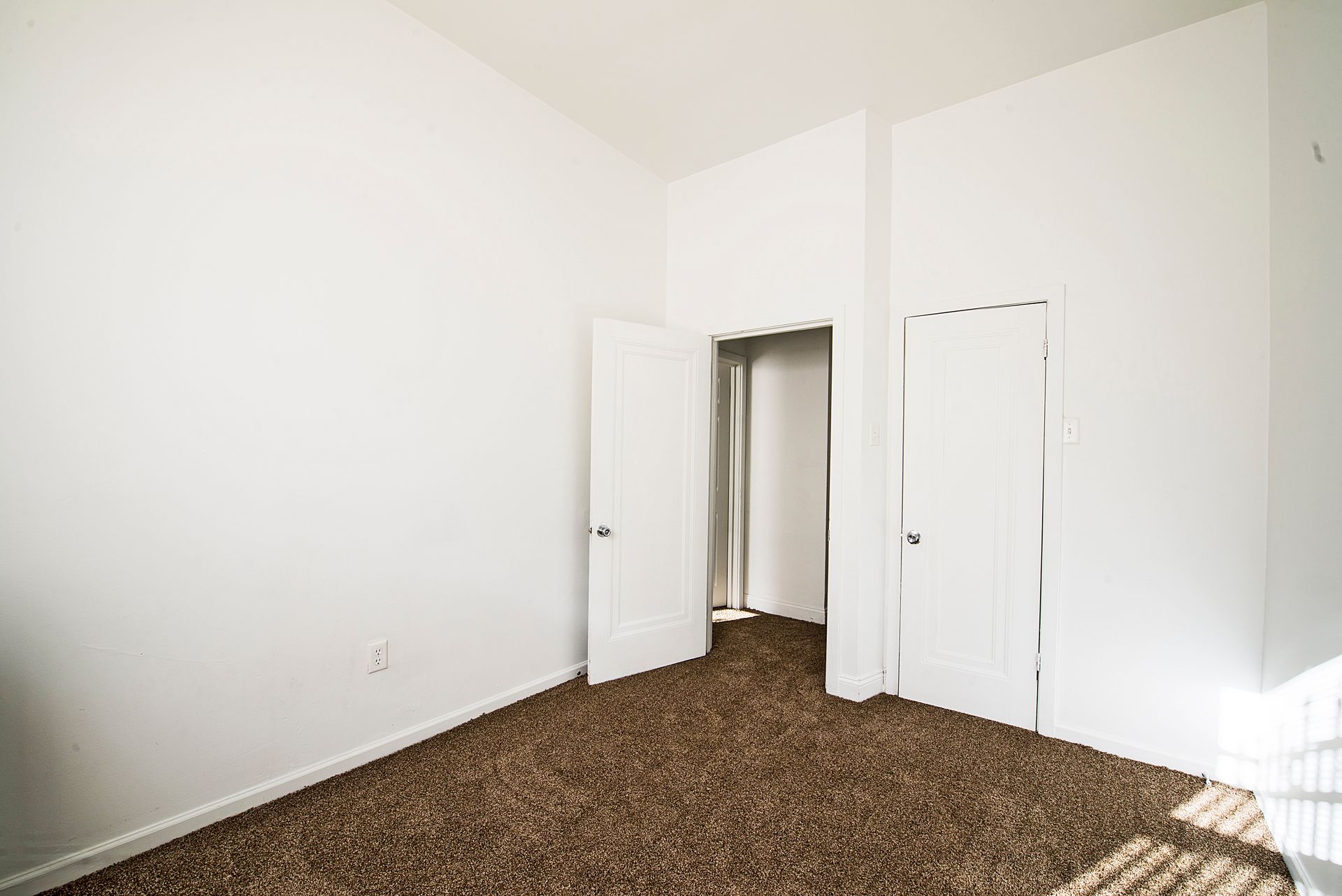 Empty room with brown carpet, white walls, and two open doors.