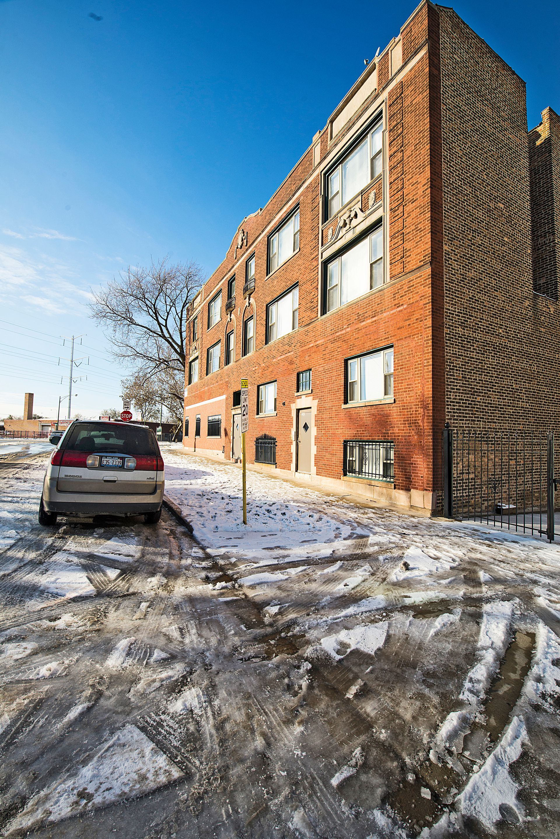 Brick apartment building on a snowy street with a car parked in front.