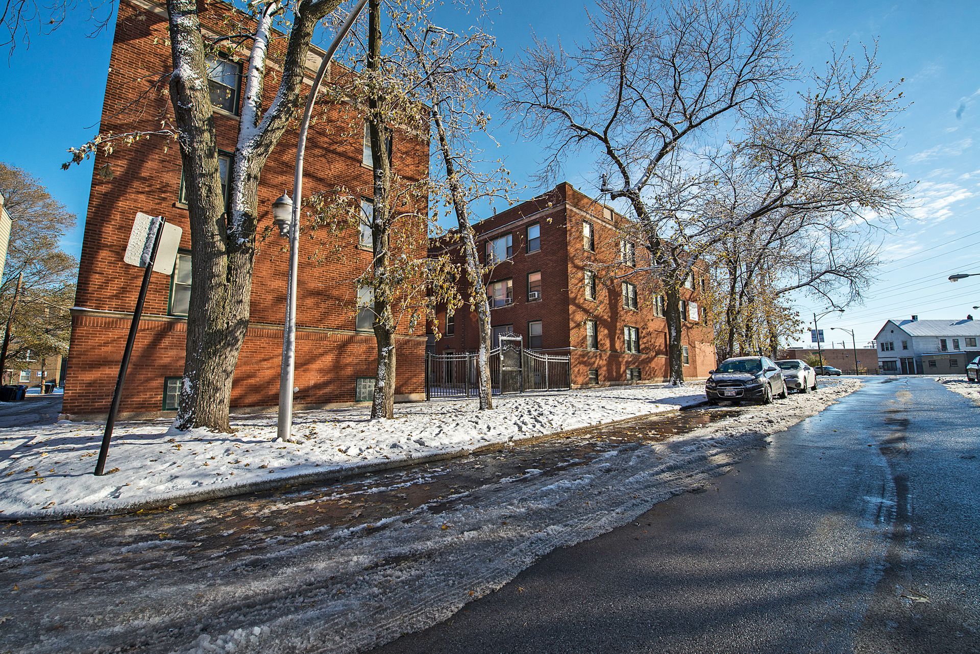 Red brick apartment buildings and bare trees line a snowy street on a sunny day.