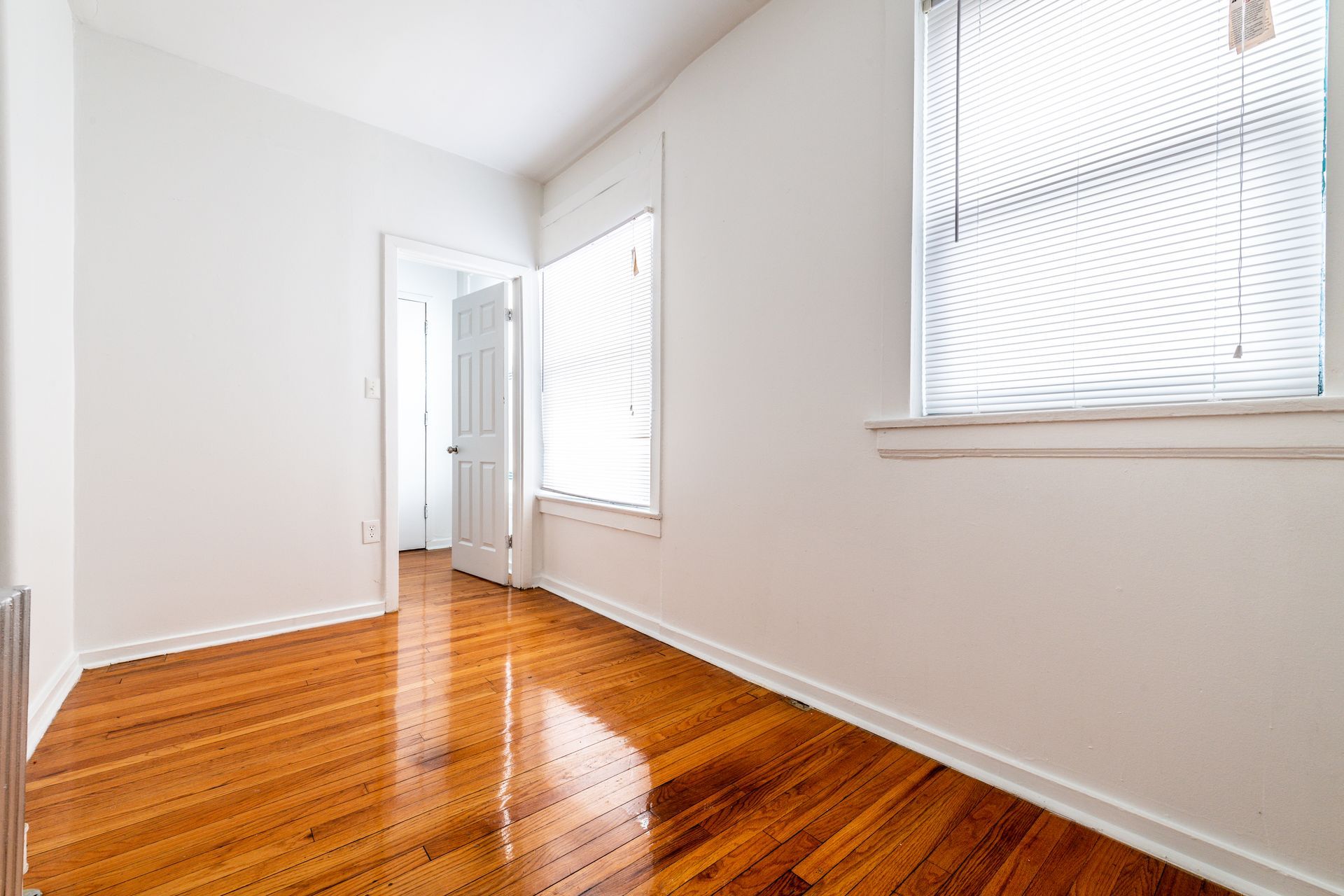 Empty room with wood floor, white walls, two windows, and an open doorway.