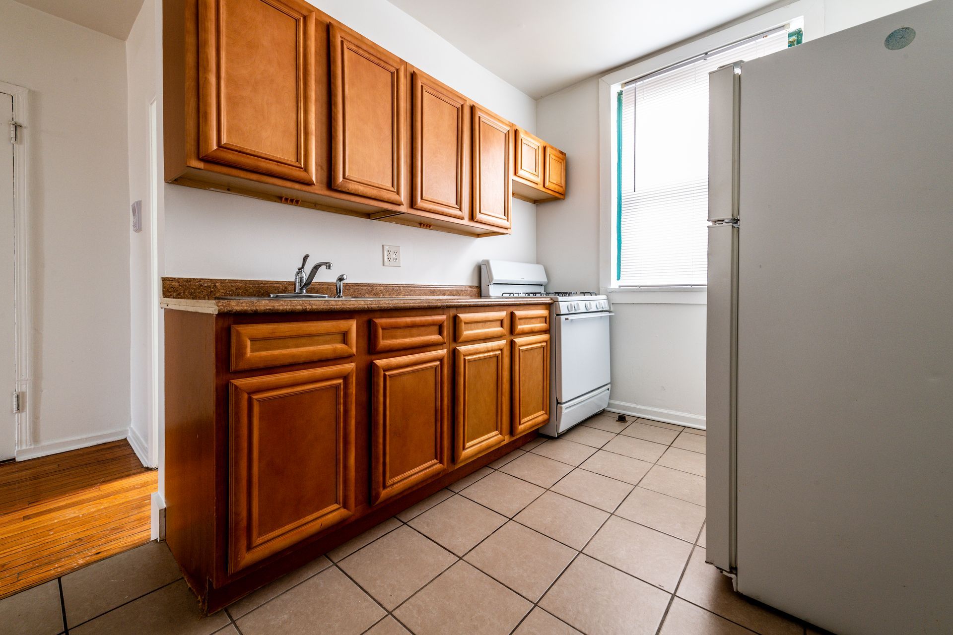 Kitchen with wooden cabinets, white appliances, and tiled floor.