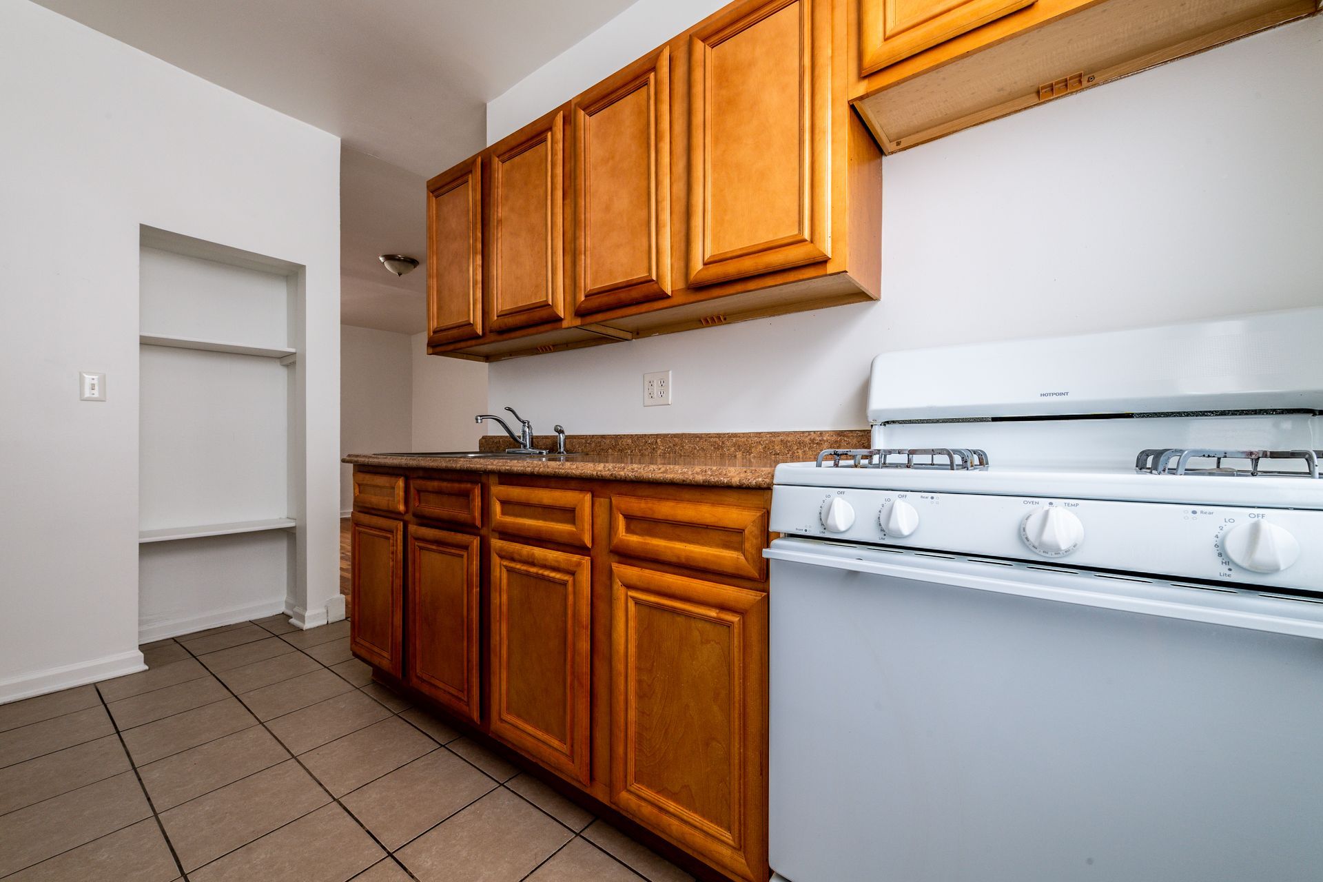 Kitchen with wooden cabinets, white stove, sink, and tiled floor.