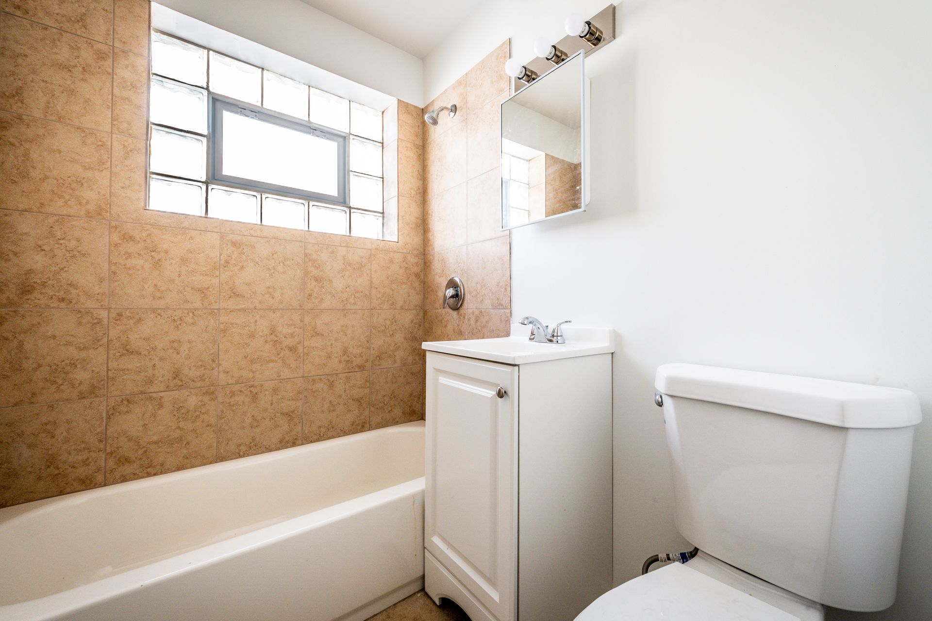 Bathroom with beige tiled wall, white fixtures, and a small window.
