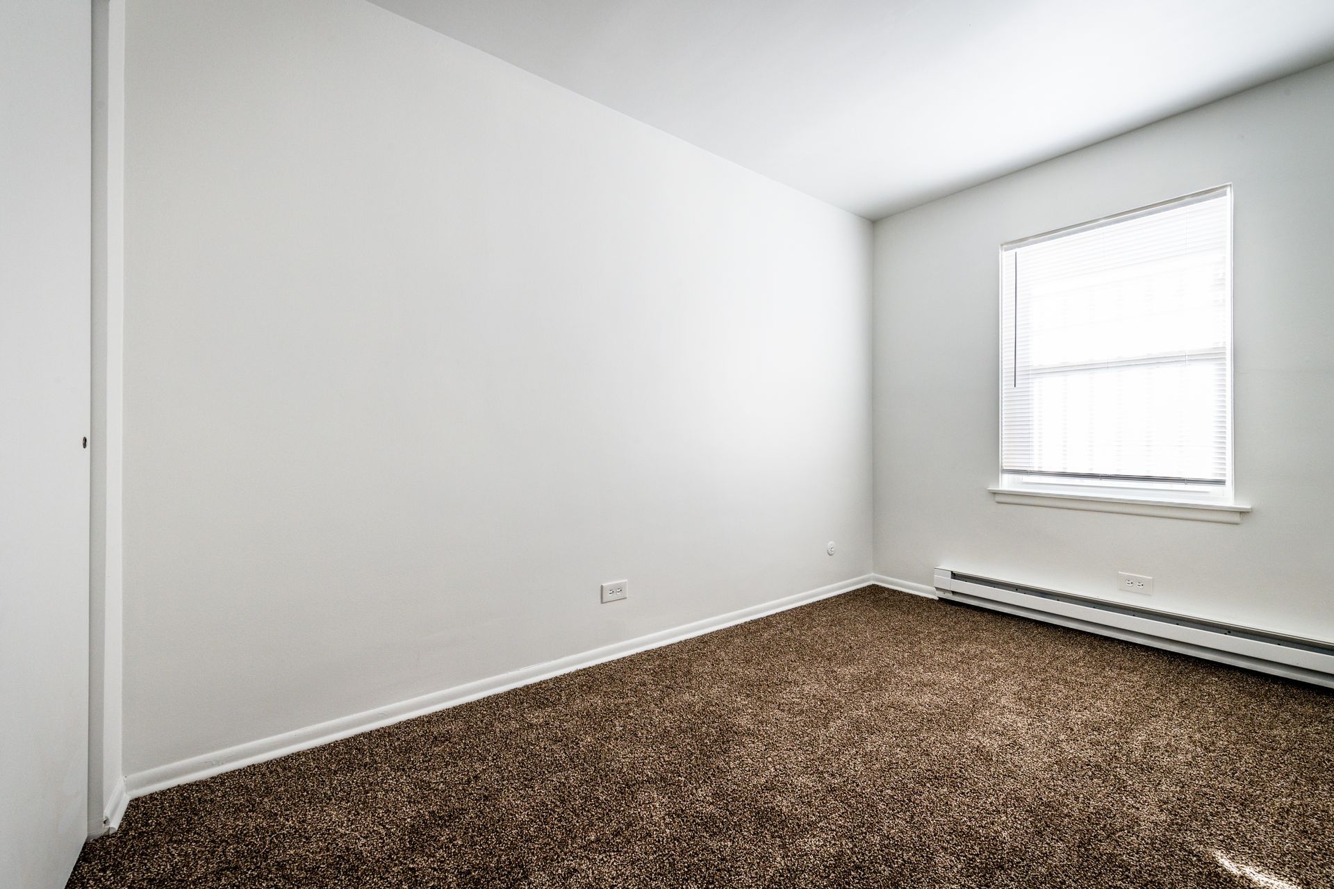 Empty room with brown carpet, white walls, a window with blinds, and a baseboard heater.