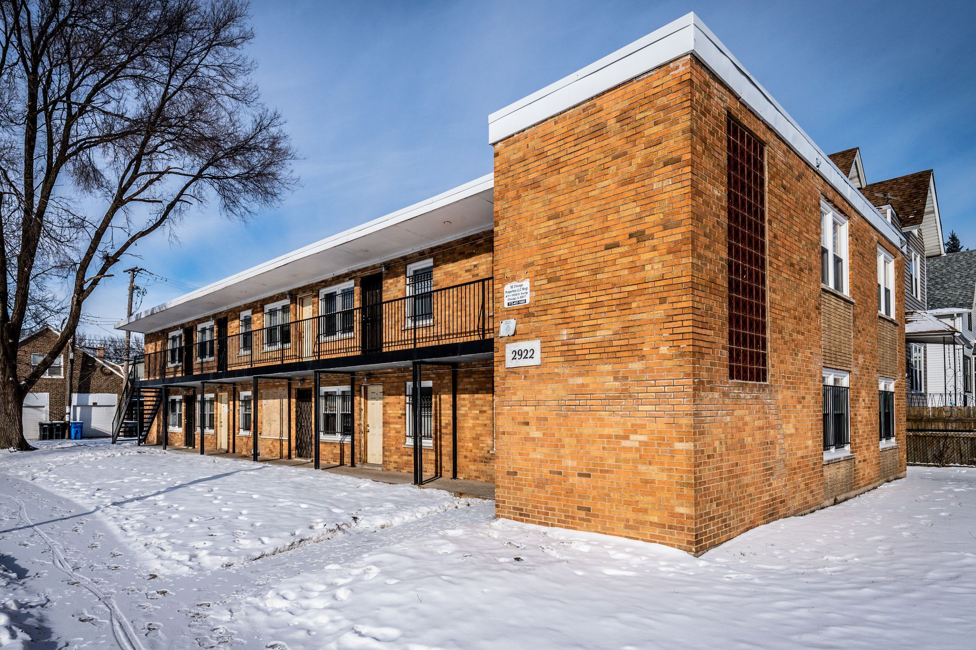 Two-story brick apartment building on a snowy day. Front facing with small balconies and white trim.