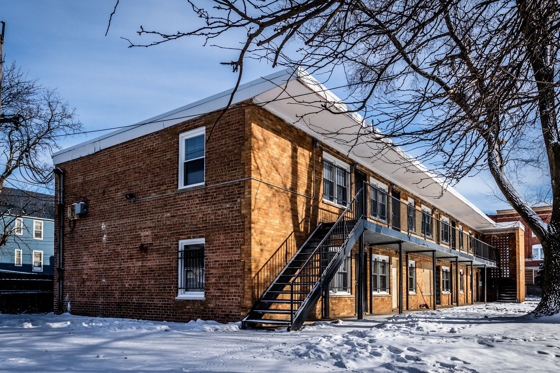 Brick apartment building in snow, with exterior staircase and bare trees.