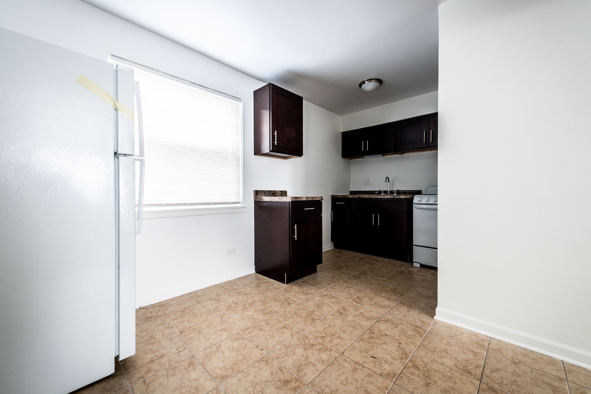 Kitchen with dark cabinets, white appliances, and tiled floor.