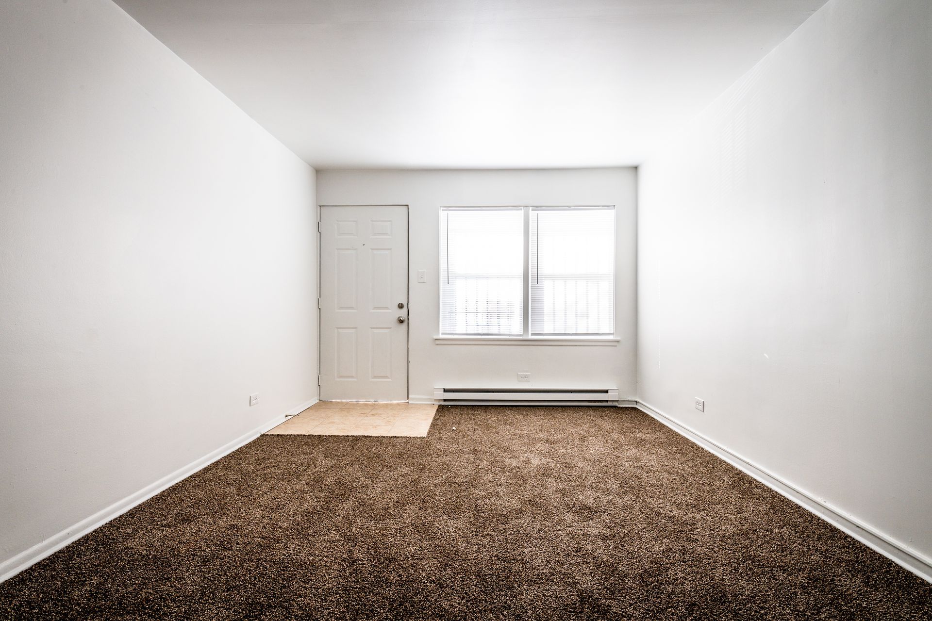 Empty room with white walls, brown carpet, window, and door.