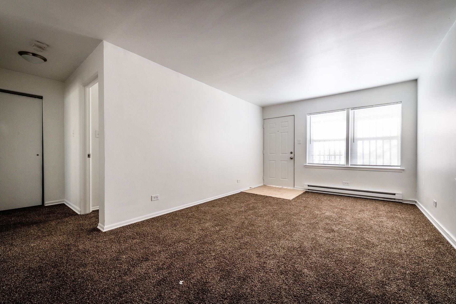 Empty room with brown carpet, white walls, and a window.