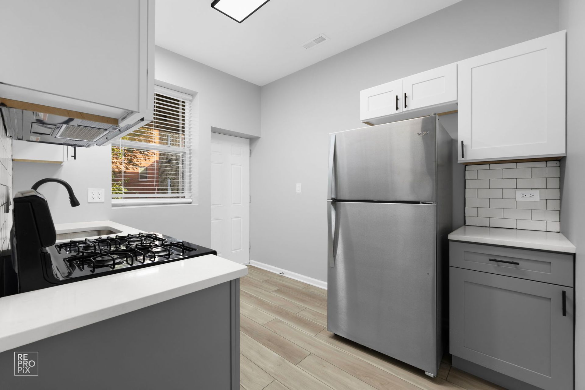 Gray and white kitchen with stainless steel refrigerator, stove, and light wood flooring.