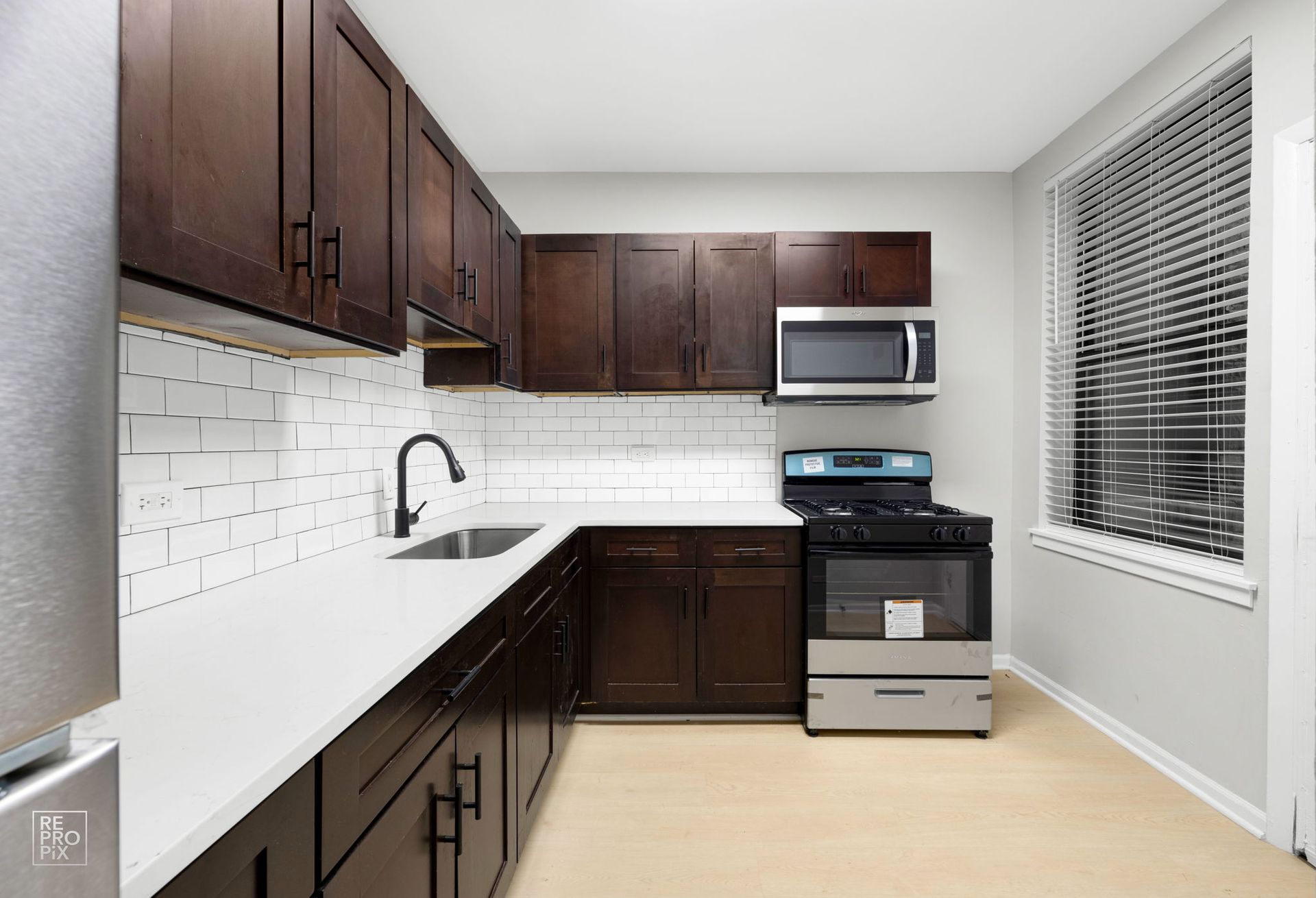 Dark wood kitchen cabinets with white countertops, stainless steel appliances, and white subway tile backsplash.