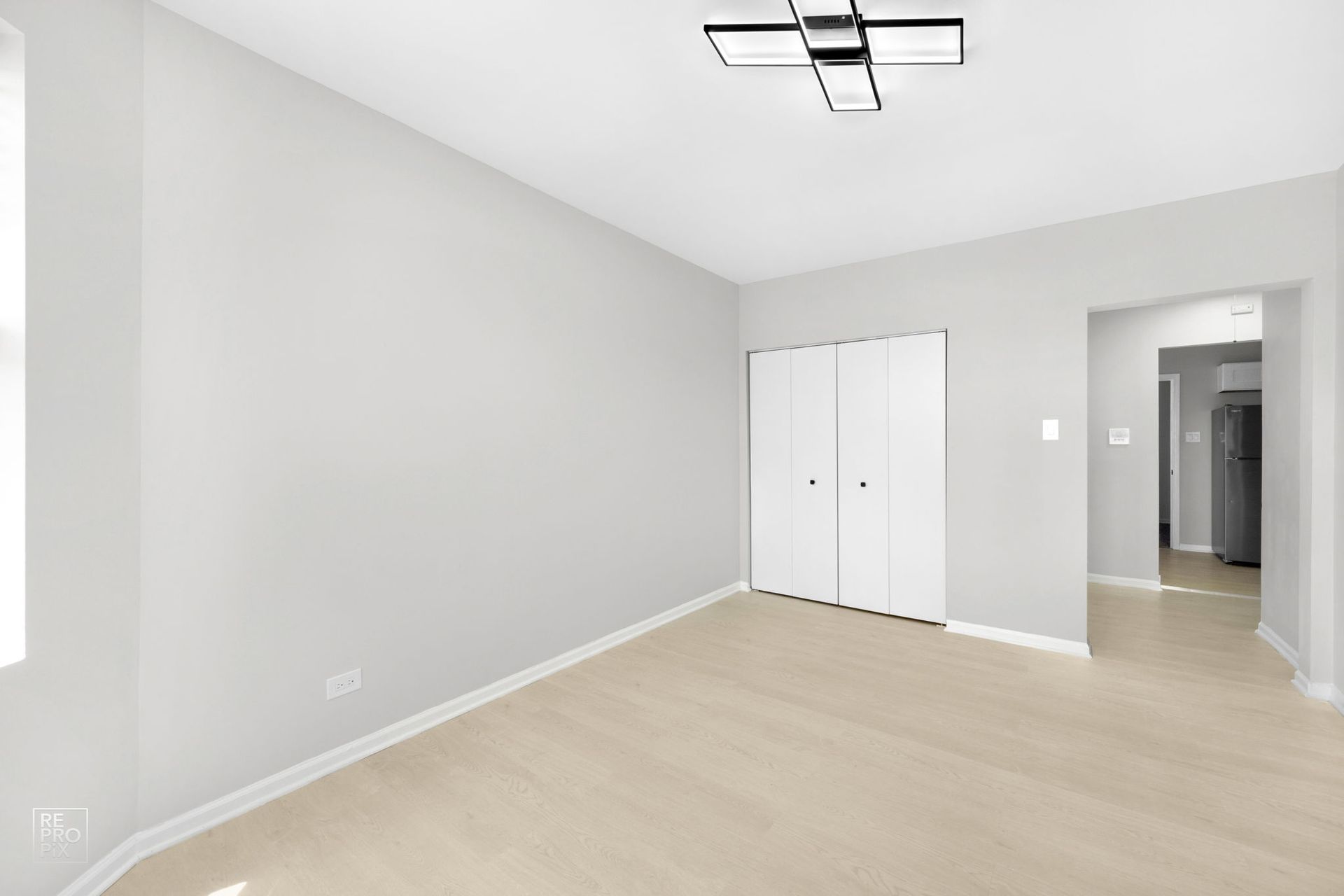 Empty room with light wood floors, white walls, closet, and doorway to another room.