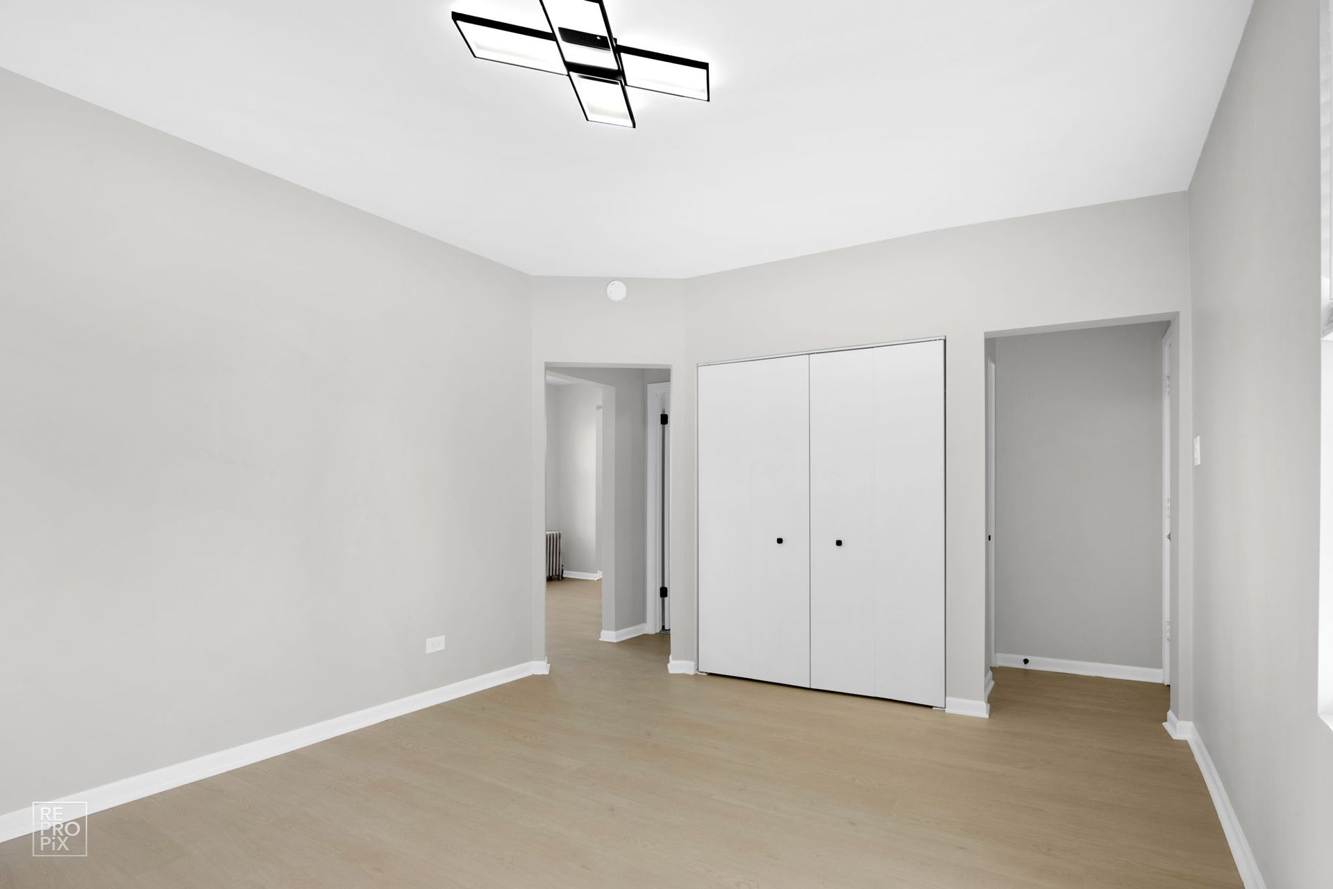 Empty room with white walls, closet, light wood floors, and ceiling light.