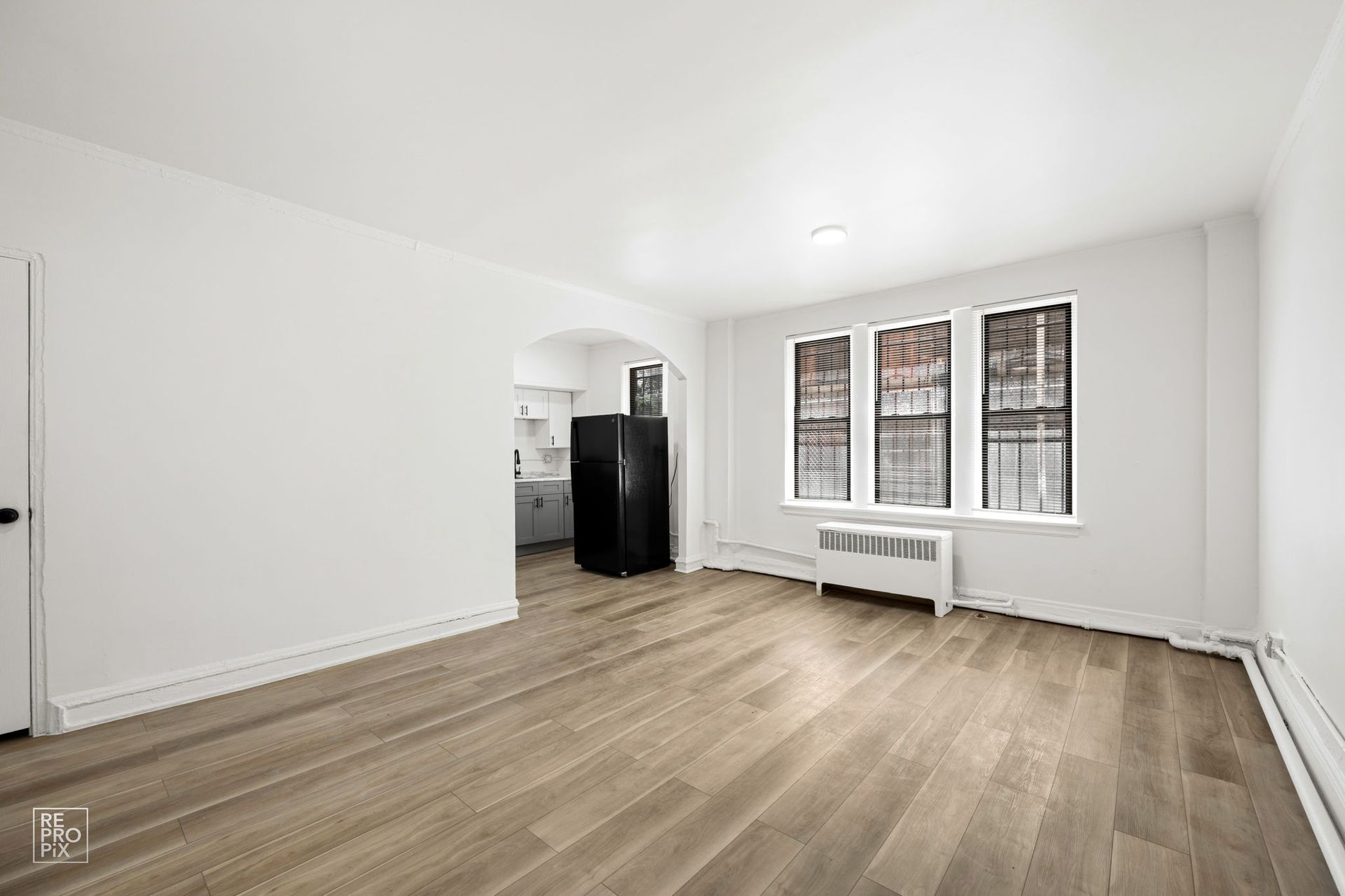 Empty apartment with light wood floors, white walls, and a large window.
