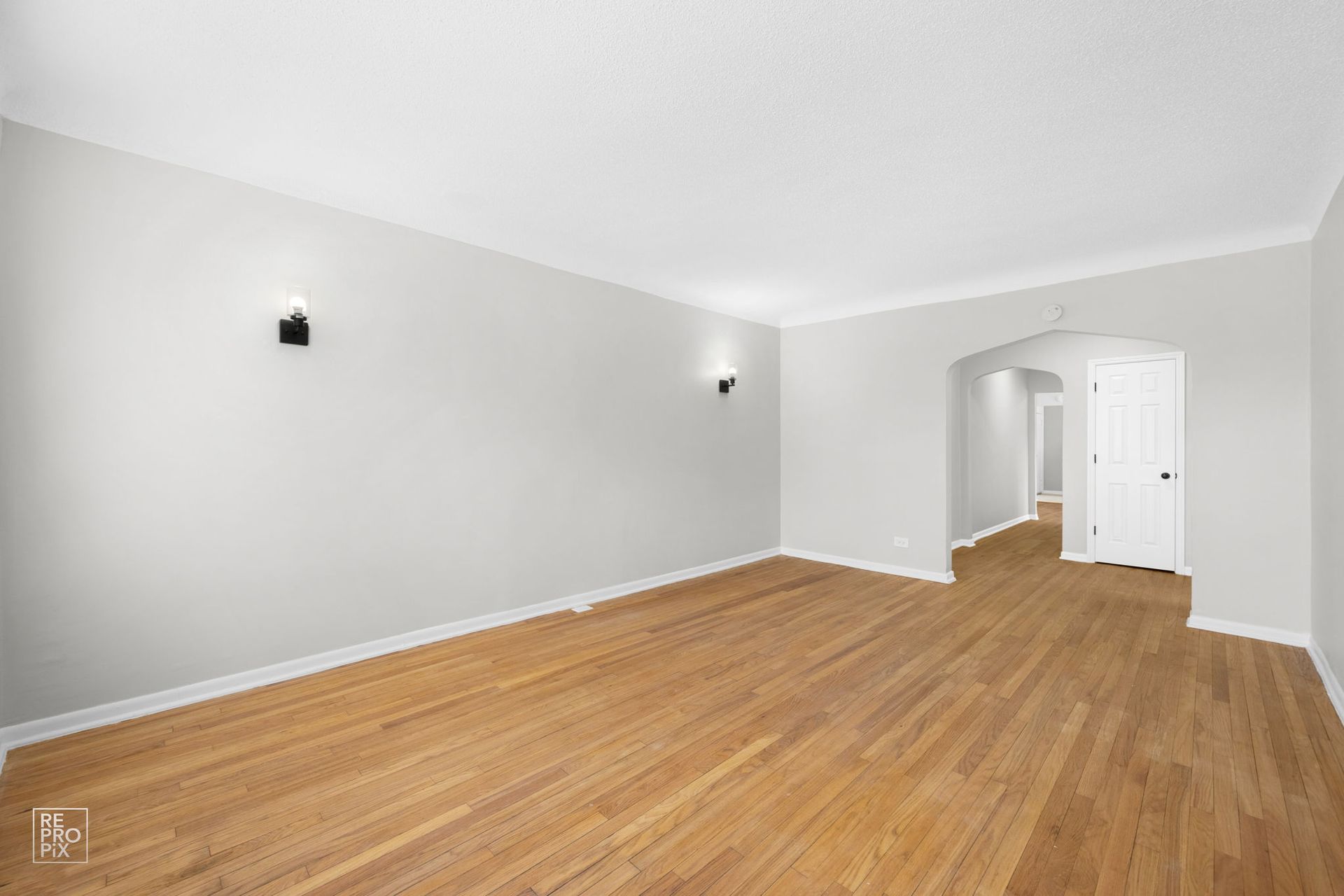 Empty room with hardwood floors, white walls, and recessed lighting.