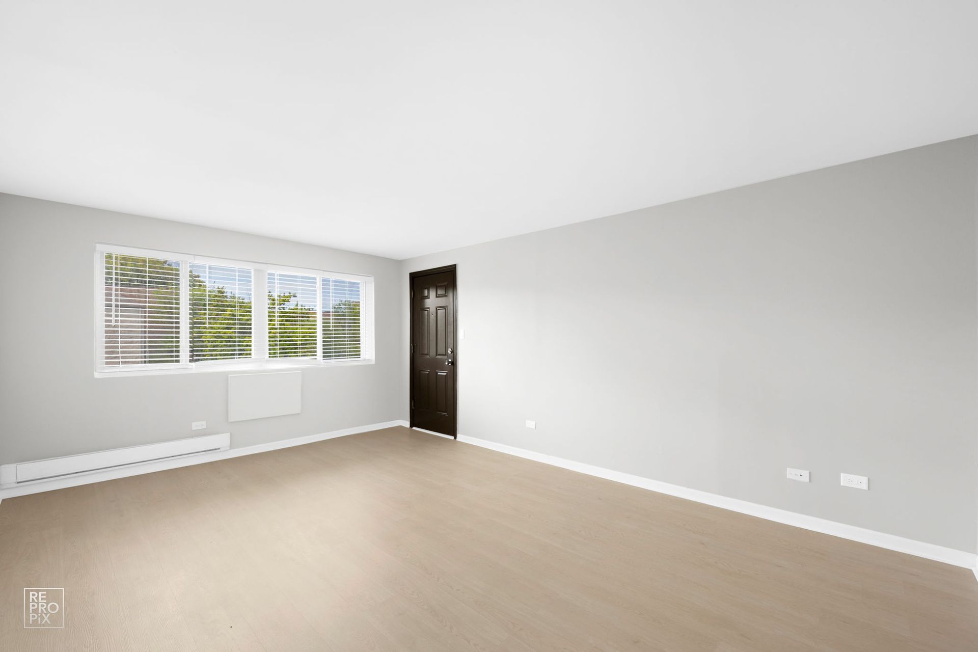 Empty living room with light wood floors, gray walls, and a window.