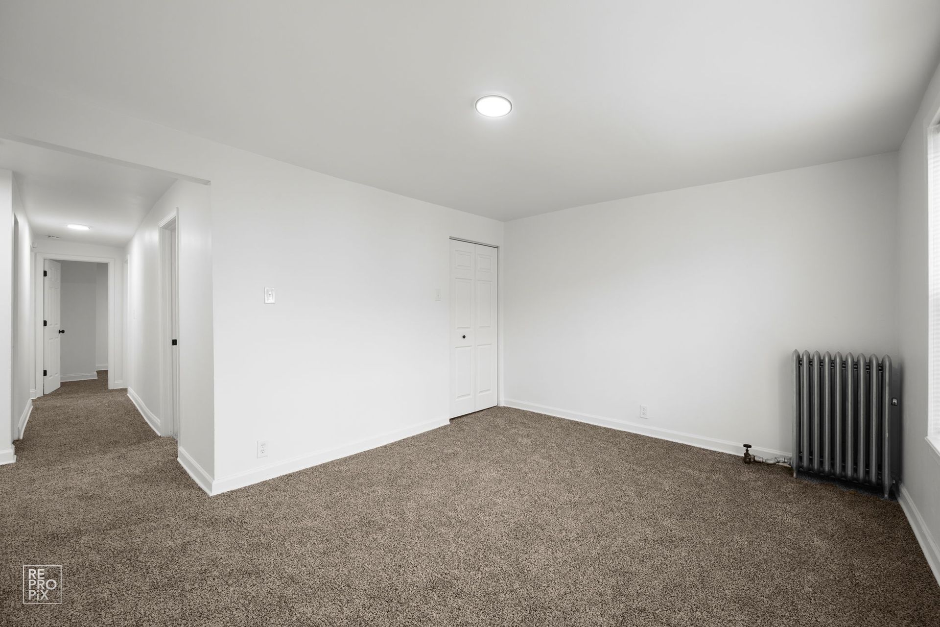 Empty room with brown carpet, white walls, and a radiator.