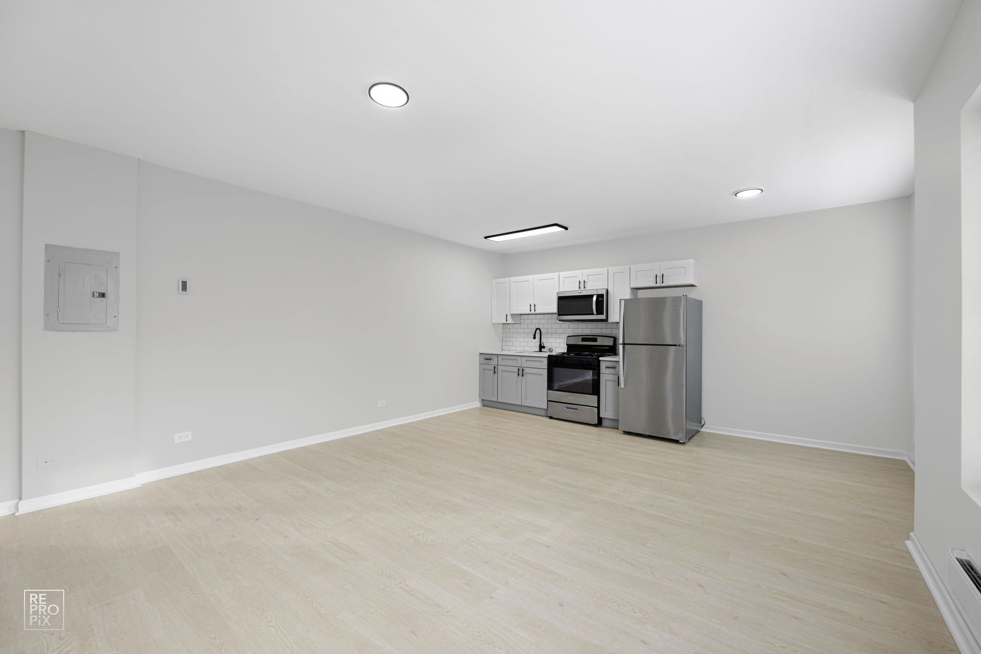 Empty studio apartment with kitchen appliances, light wood floors, and bright walls.