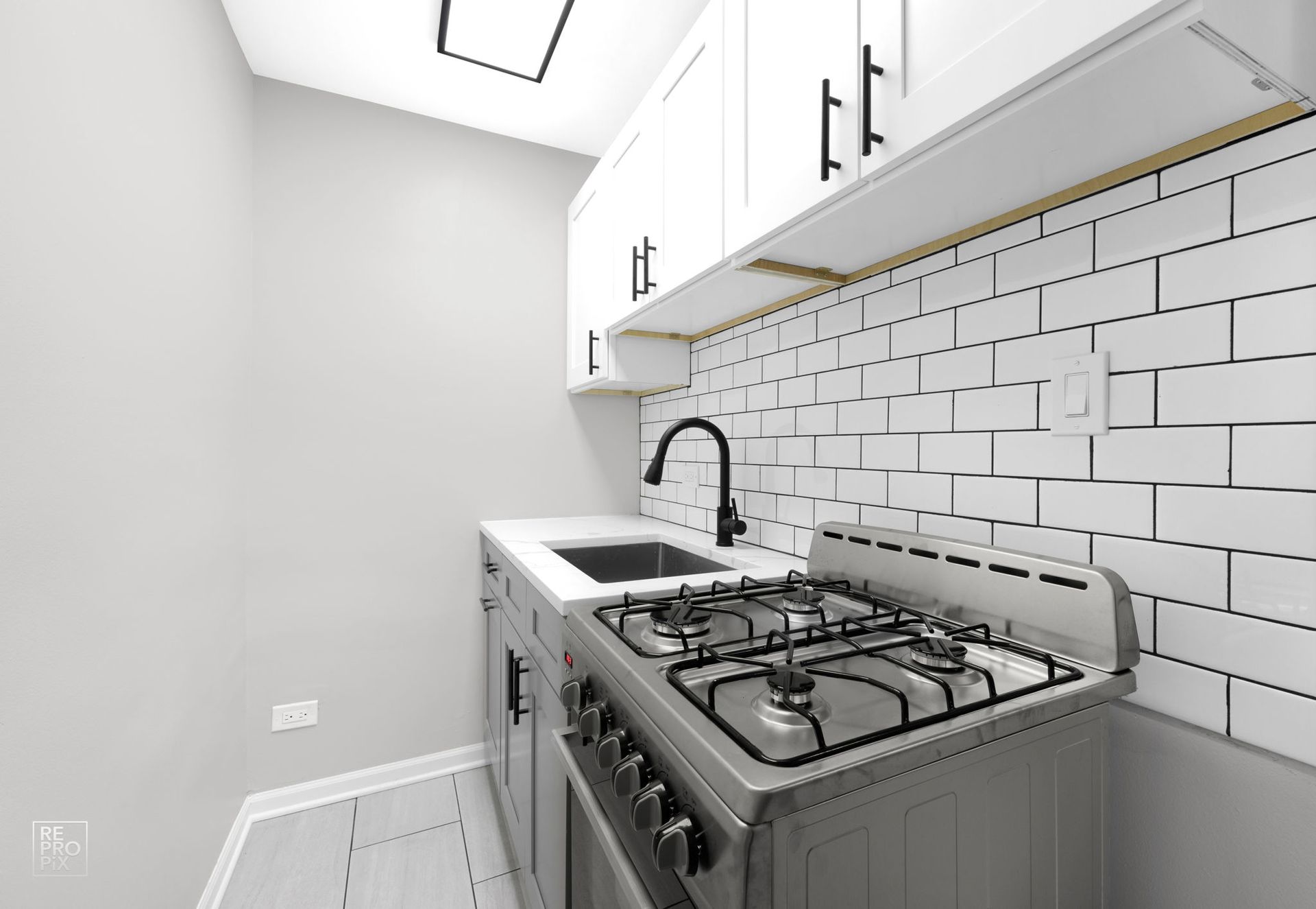 Small kitchen with stove, sink, white cabinets, and subway tile backsplash.
