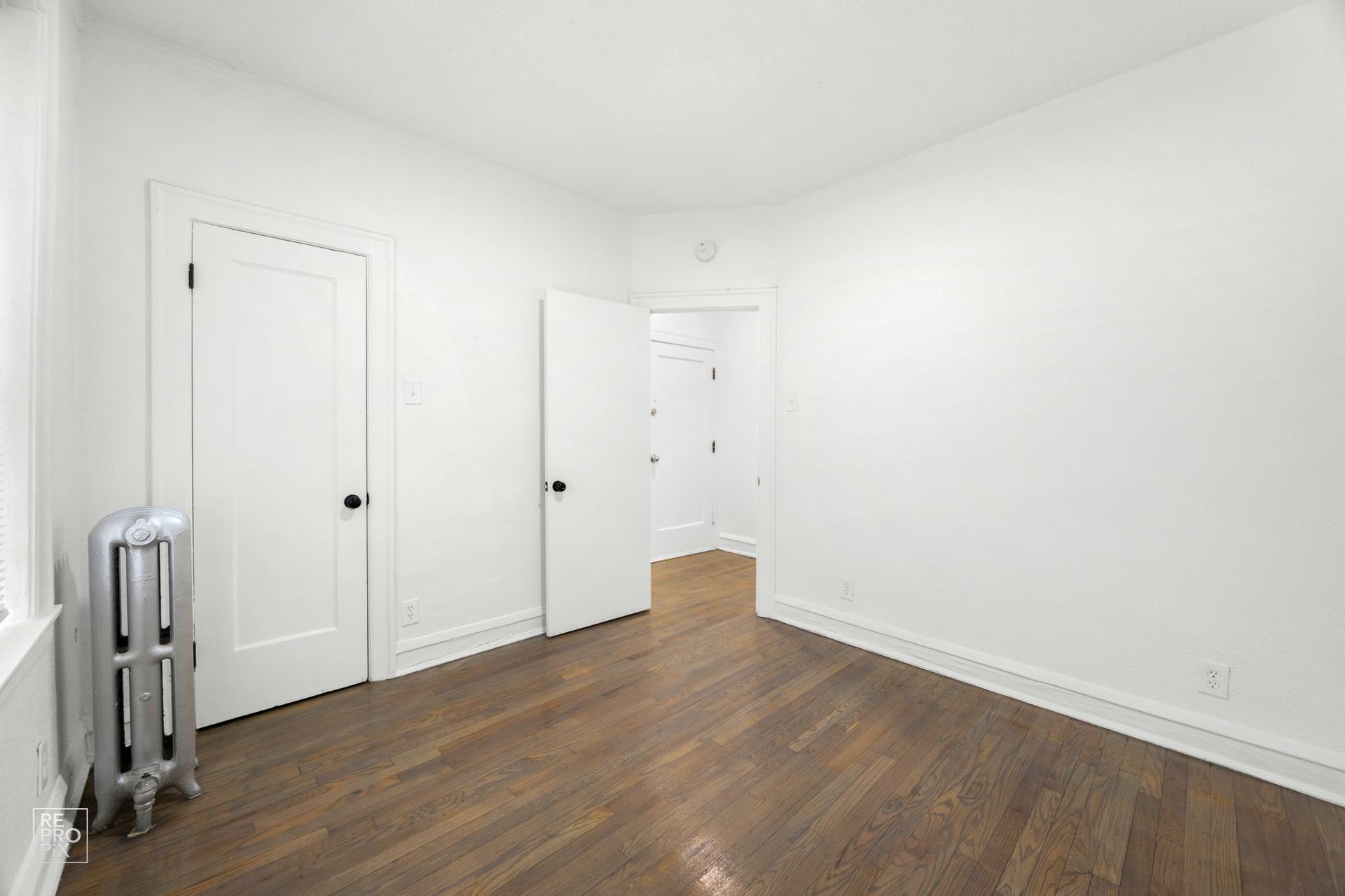 Empty room with hardwood floors, white walls, and three doorways.