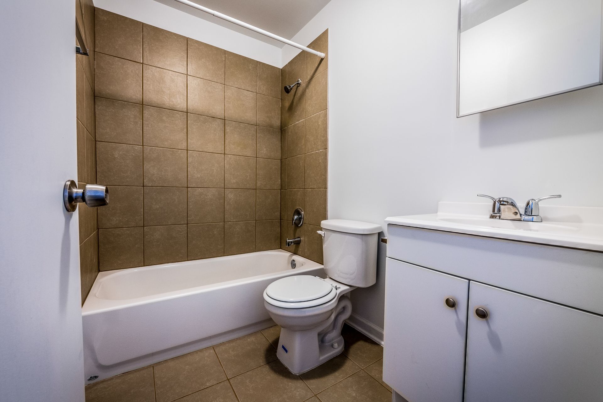 Bathroom with tub, toilet, and vanity with a mirror. Beige tile and white fixtures.
