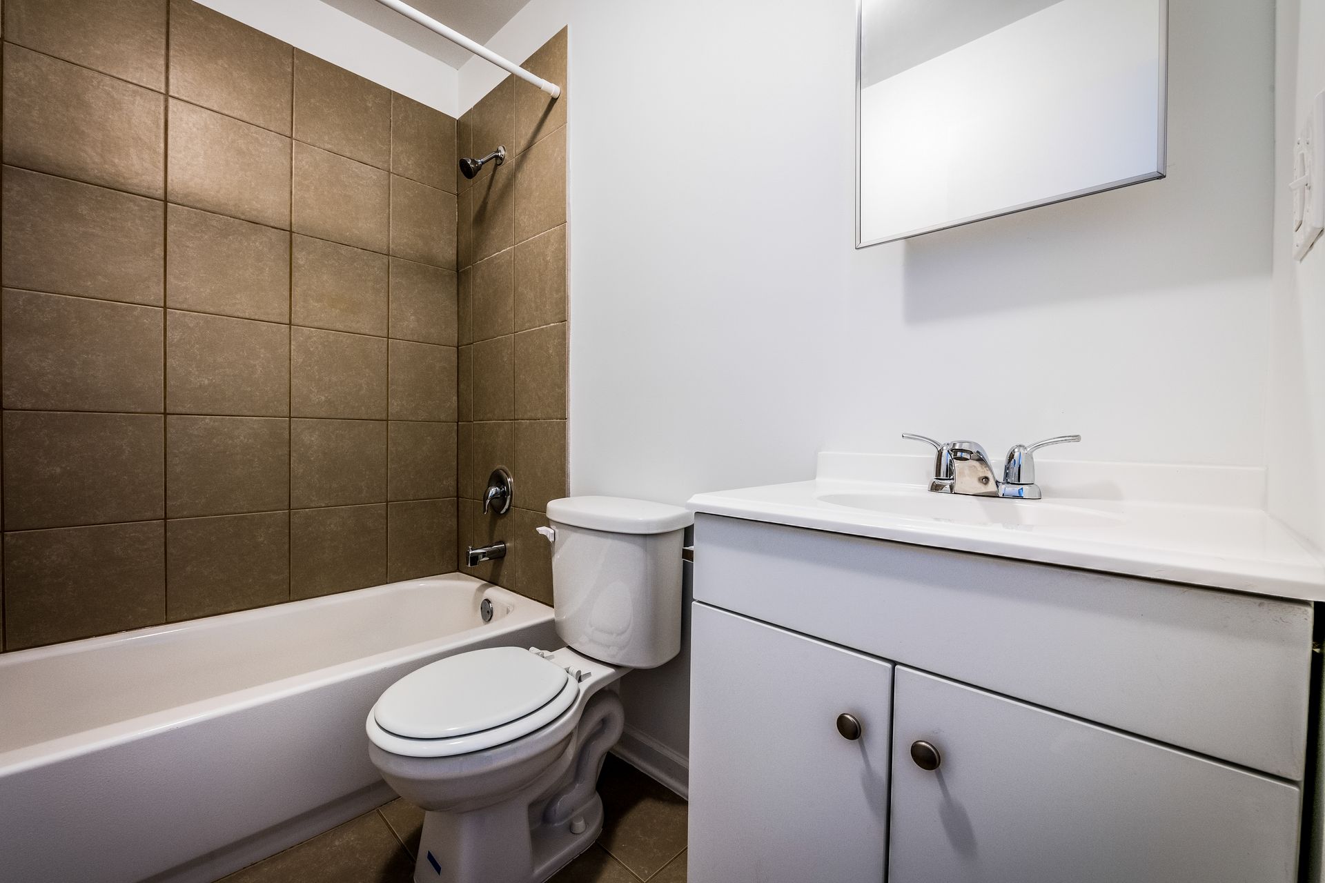 Bathroom with white fixtures, beige tile in the shower, and a white vanity with a mirror.