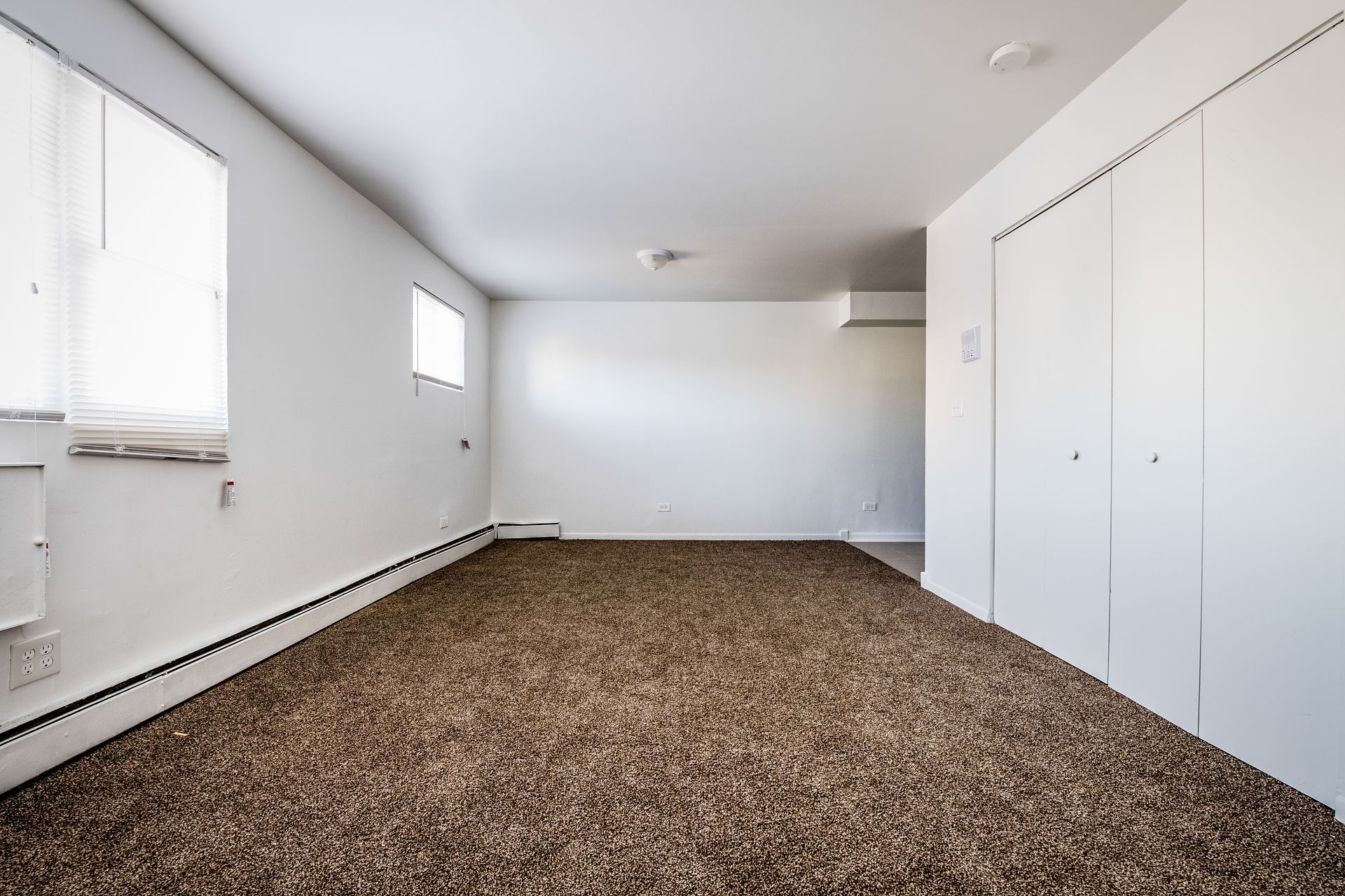 Empty room with brown carpet, white walls, two windows, and closet doors.