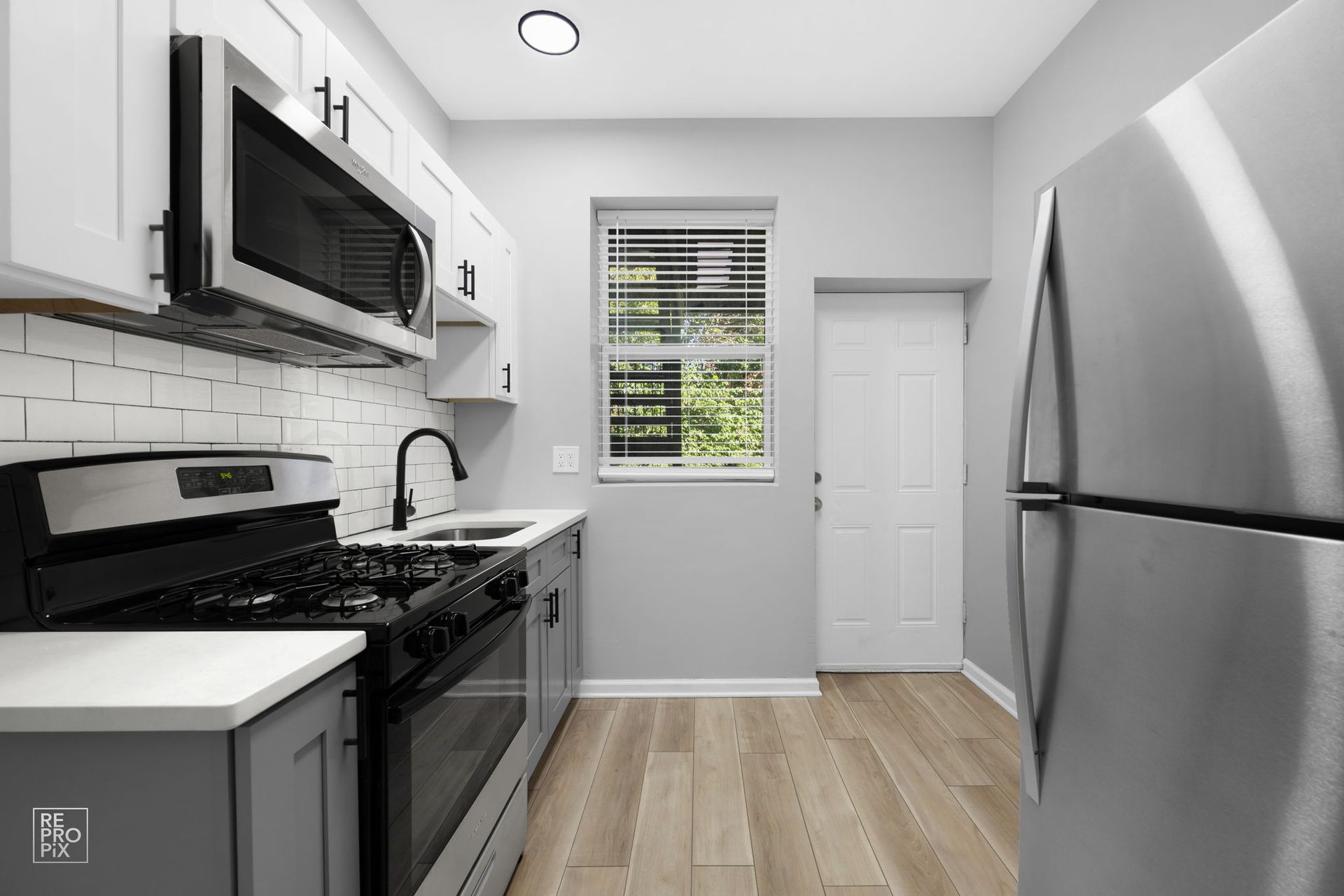 Modern kitchen with stainless steel appliances, gray and white cabinets, and wood-look flooring.