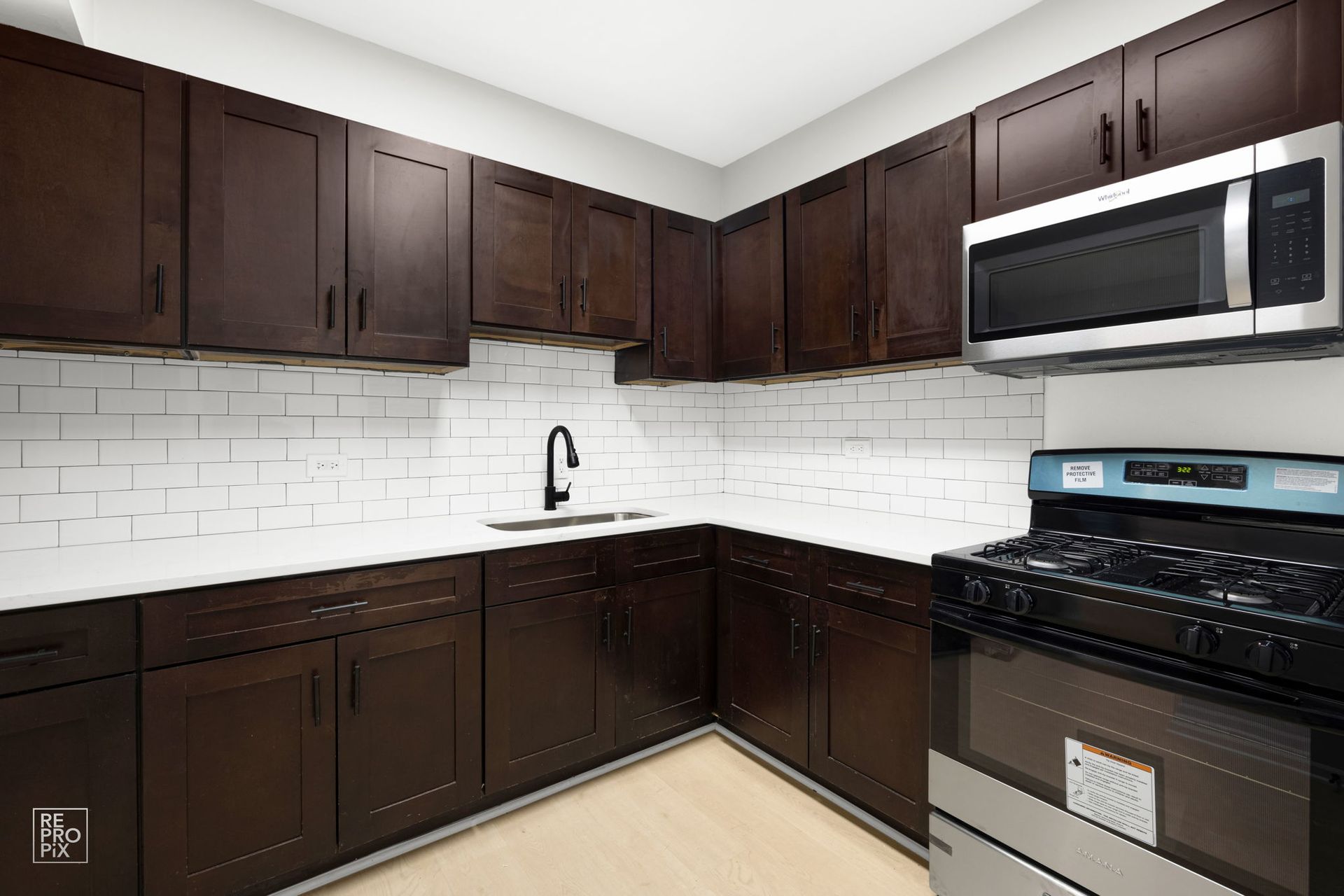 Dark brown kitchen cabinets with a white tiled backsplash and stainless steel appliances.