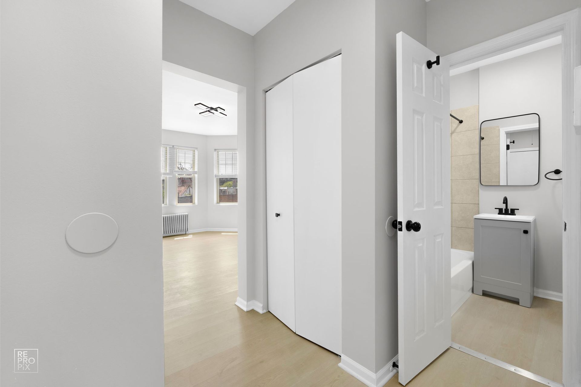 Hallway with white bi-fold doors, leading to a bathroom on the right and a light-filled room in the distance.
