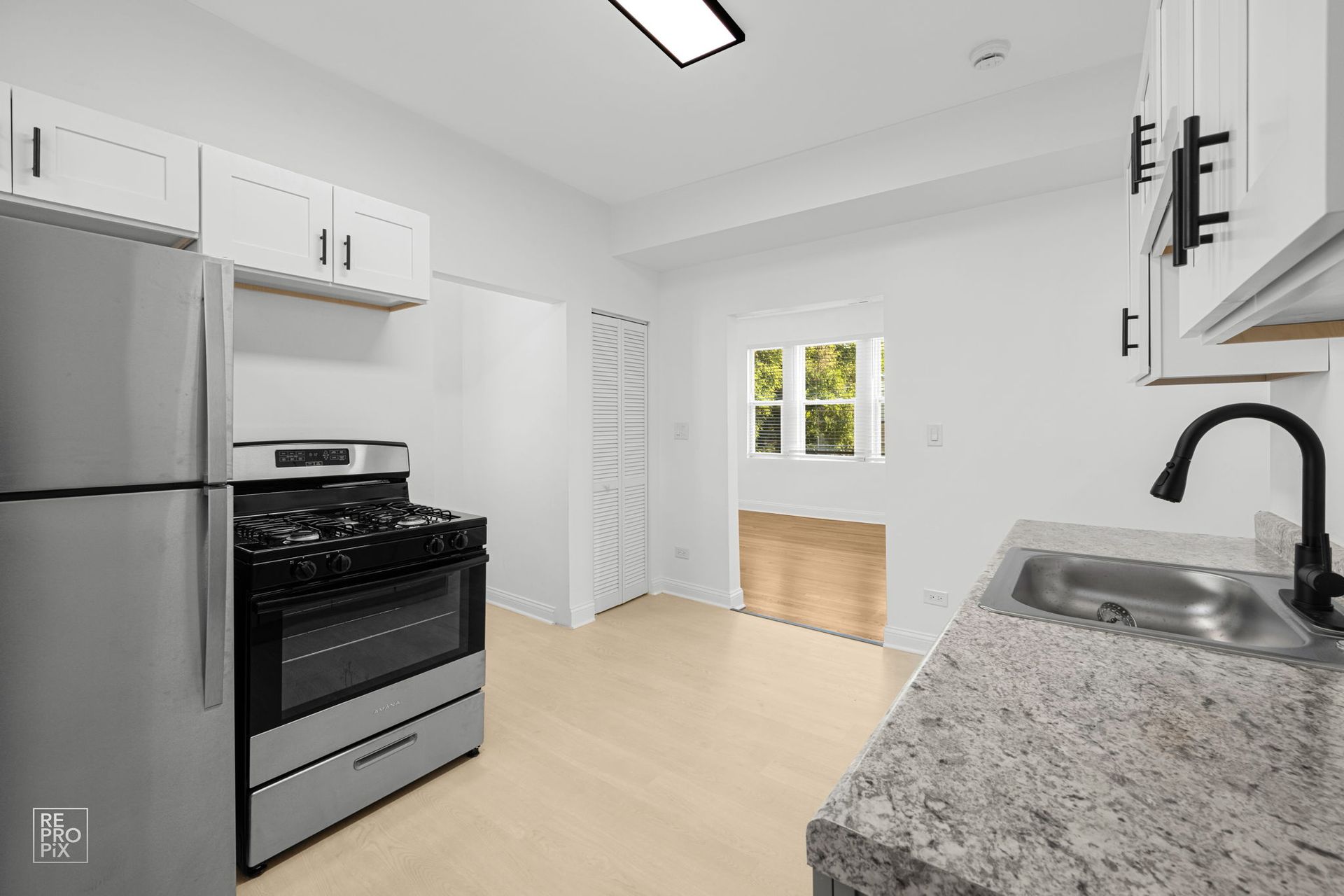 A small, bright kitchen with stainless steel appliances, light cabinets, and a doorway.
