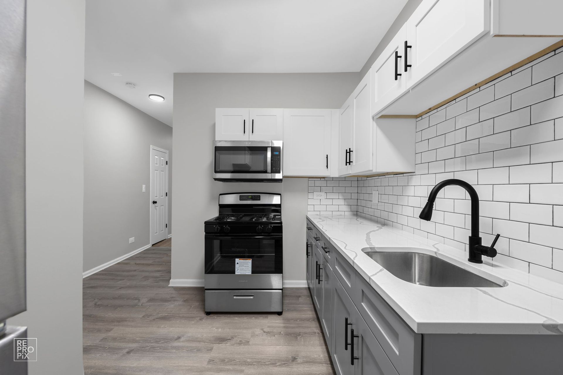 Empty room with gray walls, hardwood floor, and white trim. Doorways lead to other rooms.