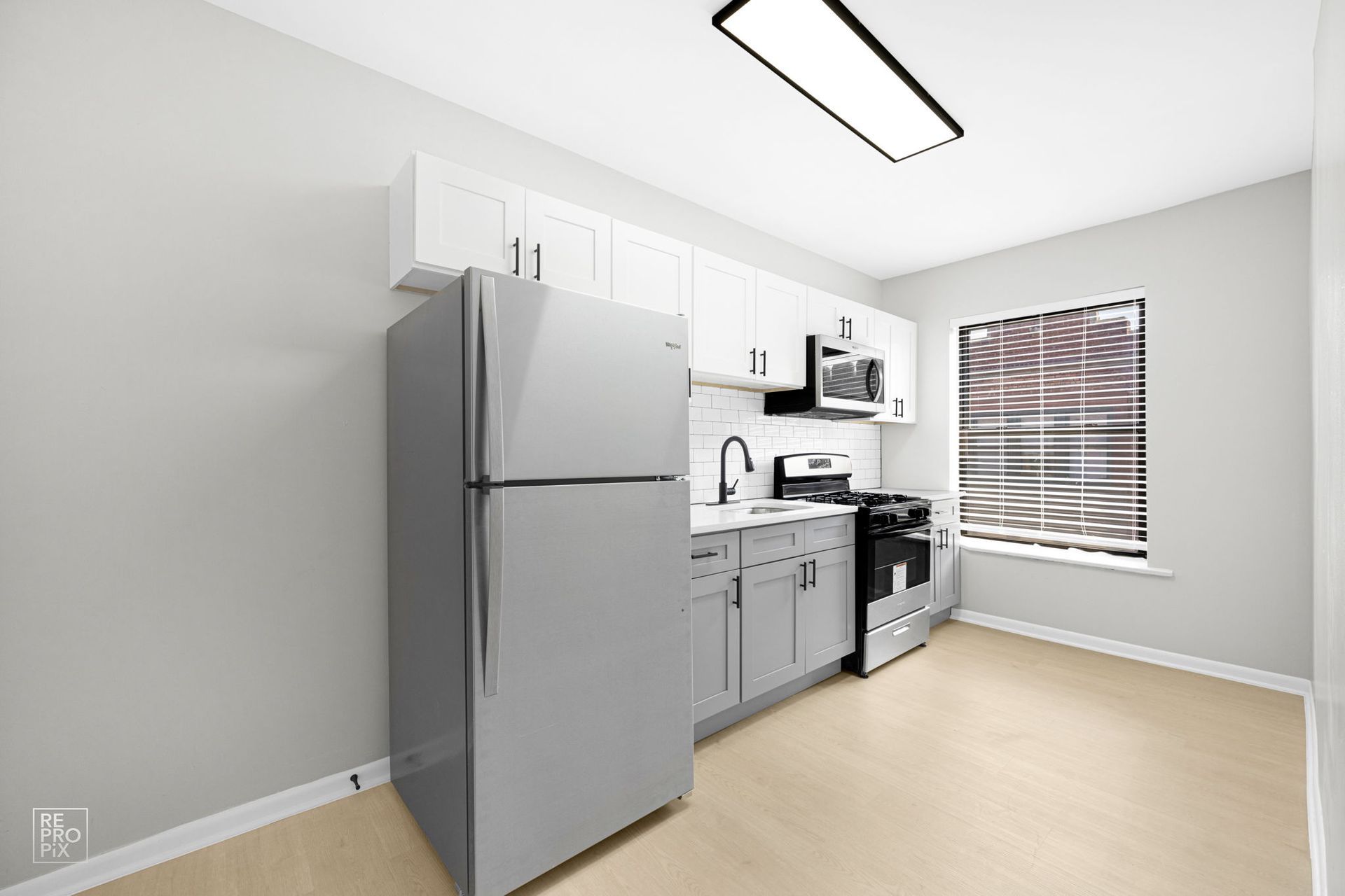 Small kitchen with white cabinets, stainless steel appliances, and a window with blinds.
