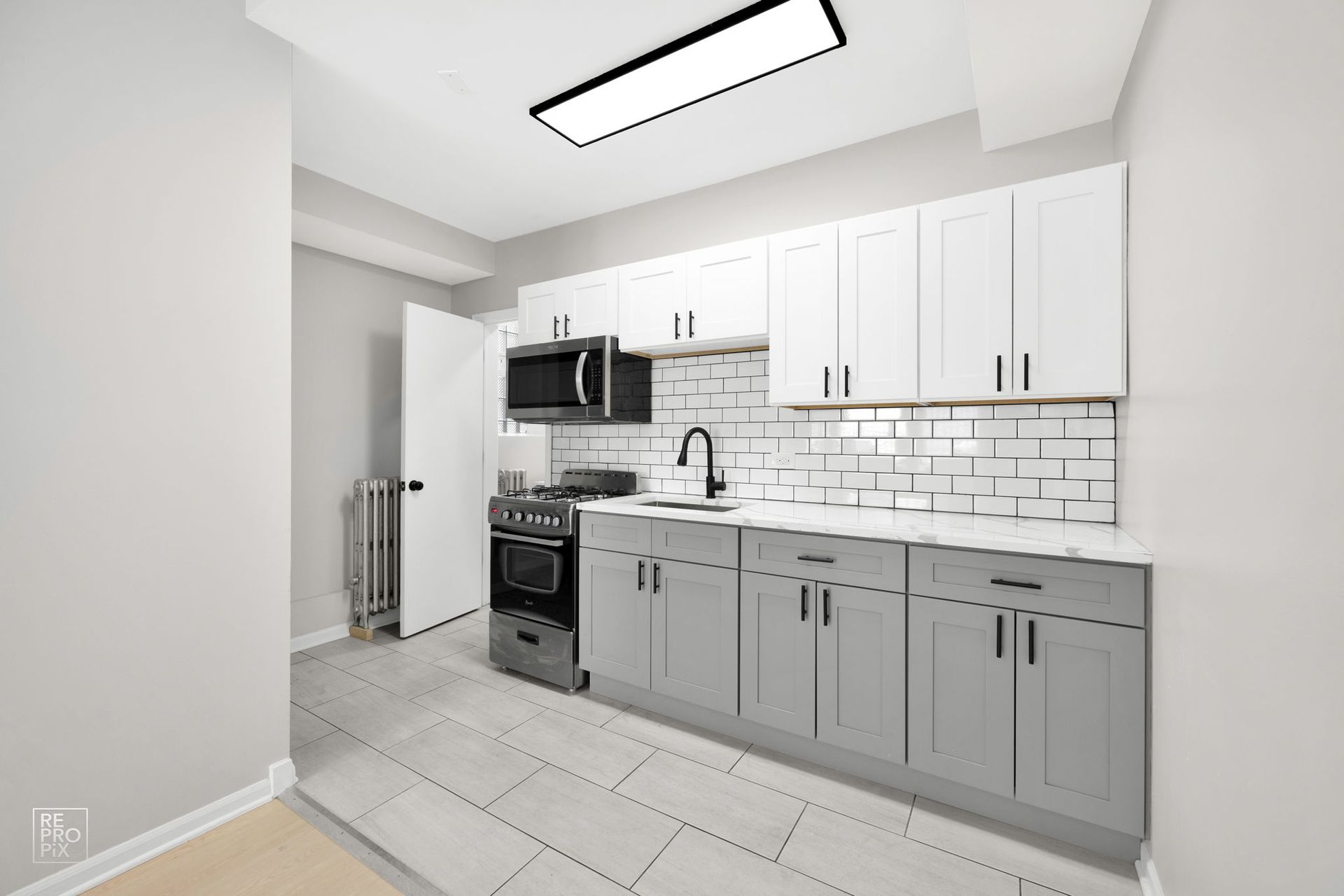 Gray and white kitchen with cabinets, stove, microwave, and sink. White brick backsplash.