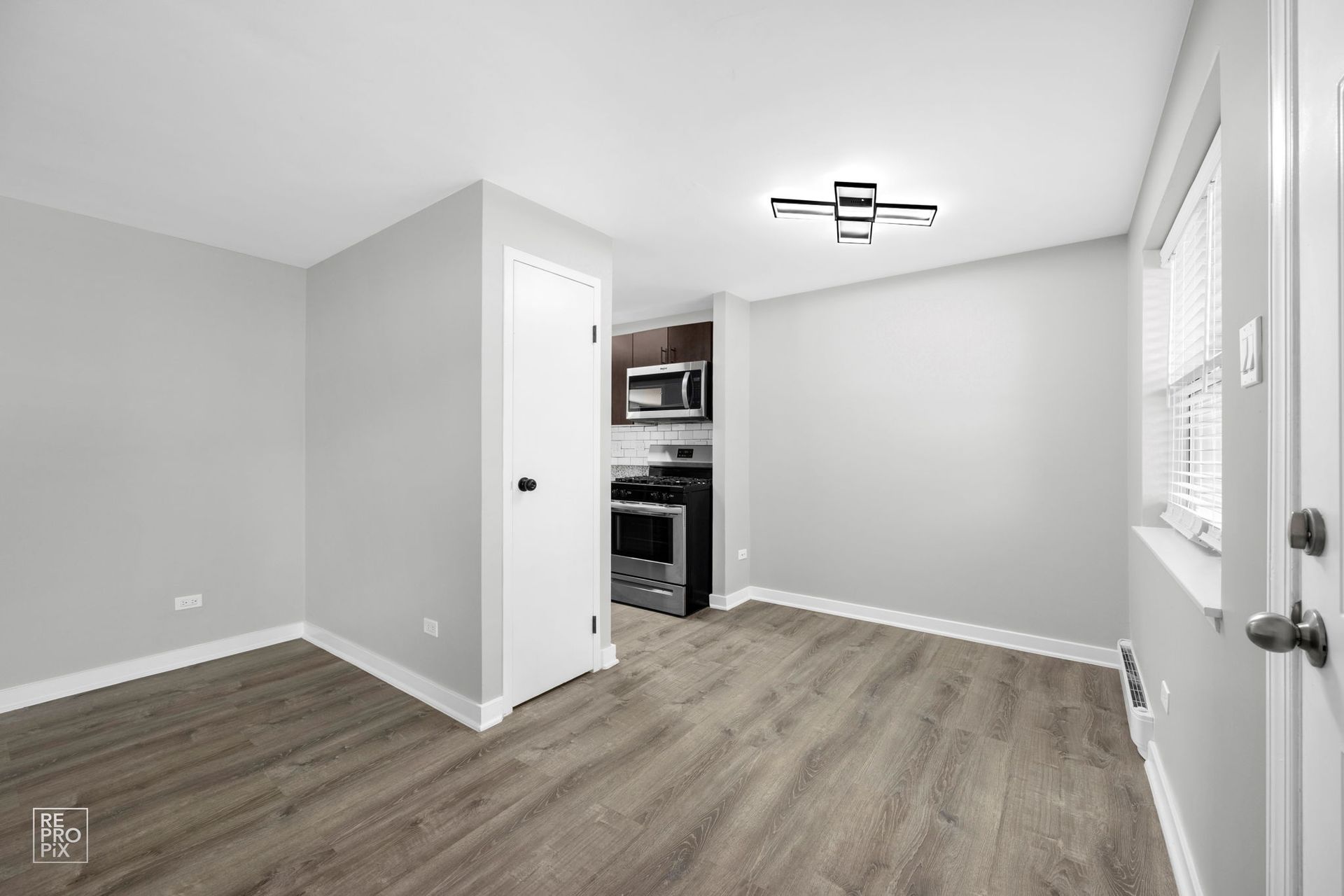 Empty apartment interior with gray walls, wood-look floor, and a small kitchen visible.