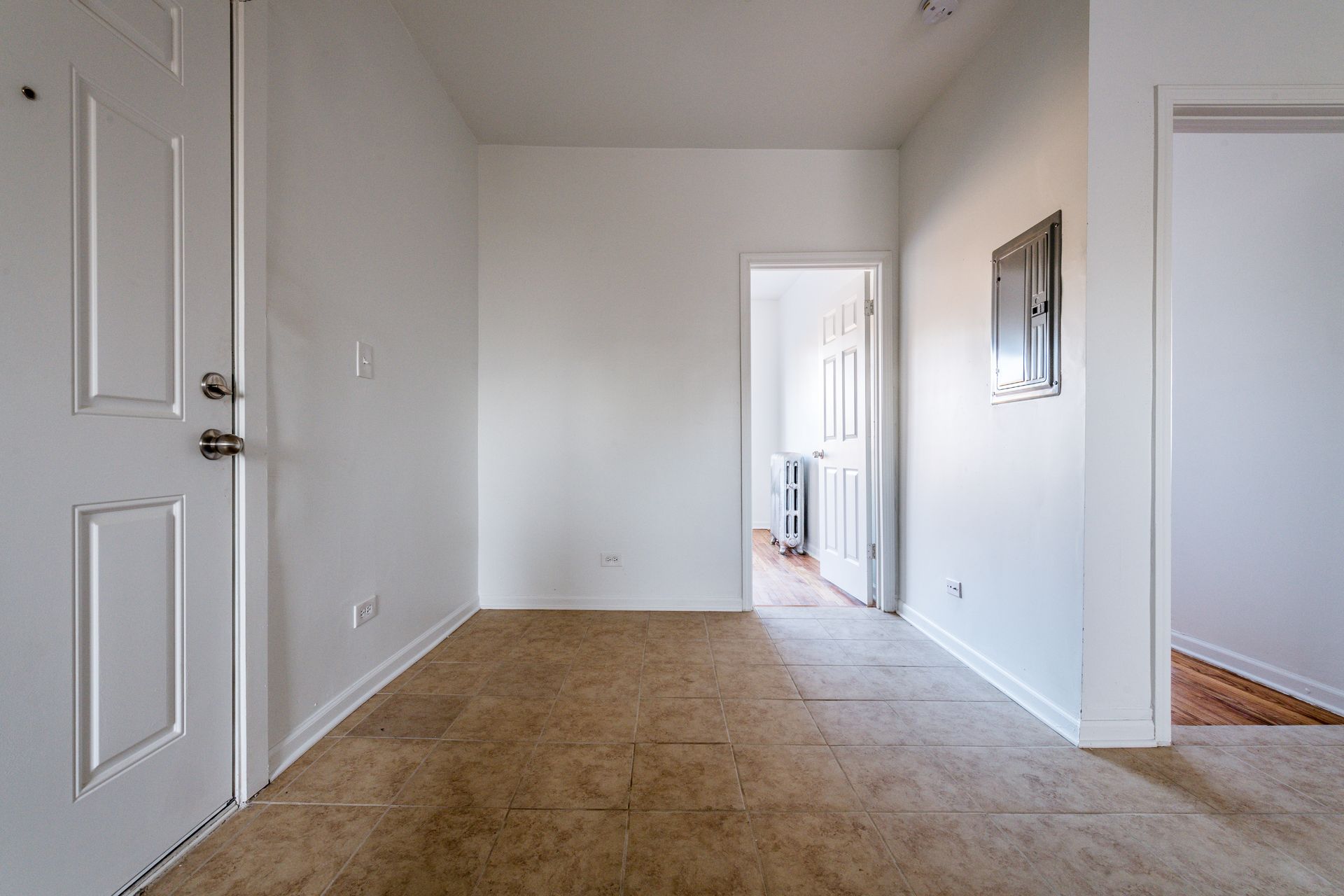 Empty room with white walls, tan carpet, doorways, and a closed white door.