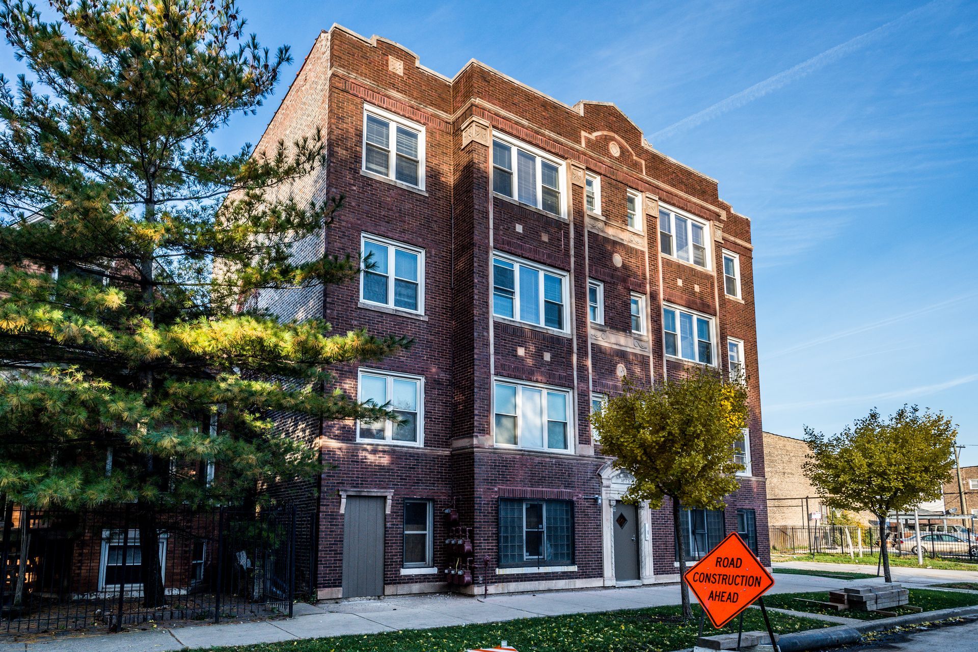 Brick apartment building on a sunny street with trees. Construction sign in front.