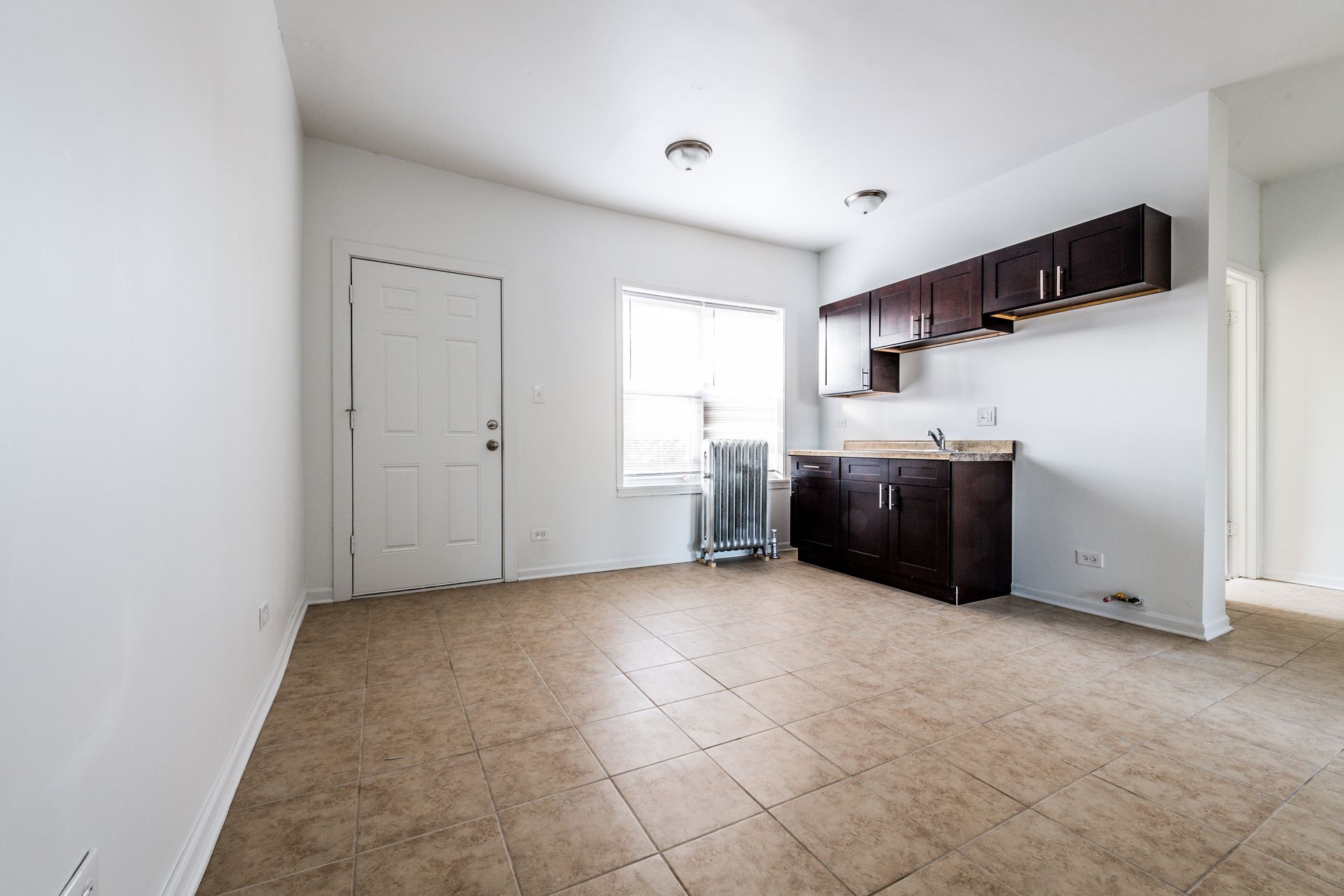 Empty studio apartment with kitchen cabinets, door, and window.