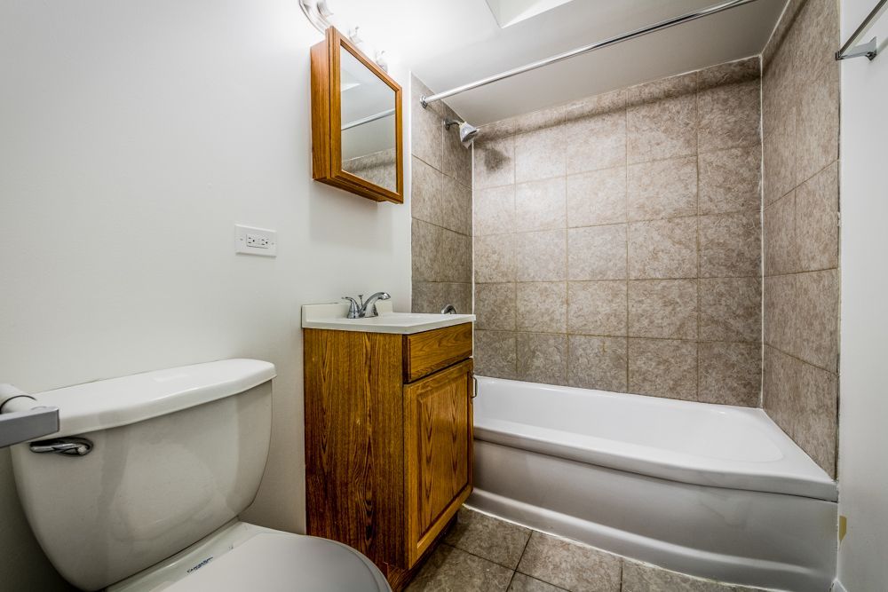 Small bathroom with white walls, toilet, vanity, and shower/tub with brown tile.