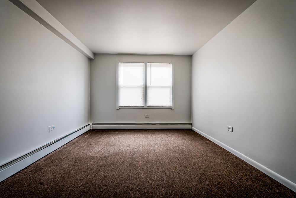 Empty room with brown carpet, white walls, and a window with blinds.