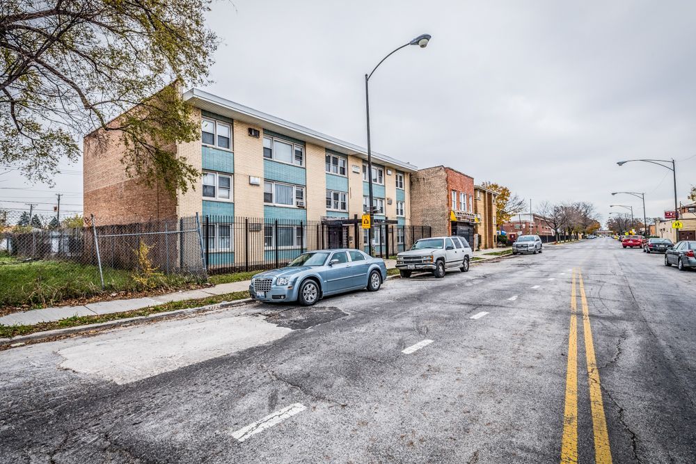Apartment building on a street with parked cars and overcast sky.