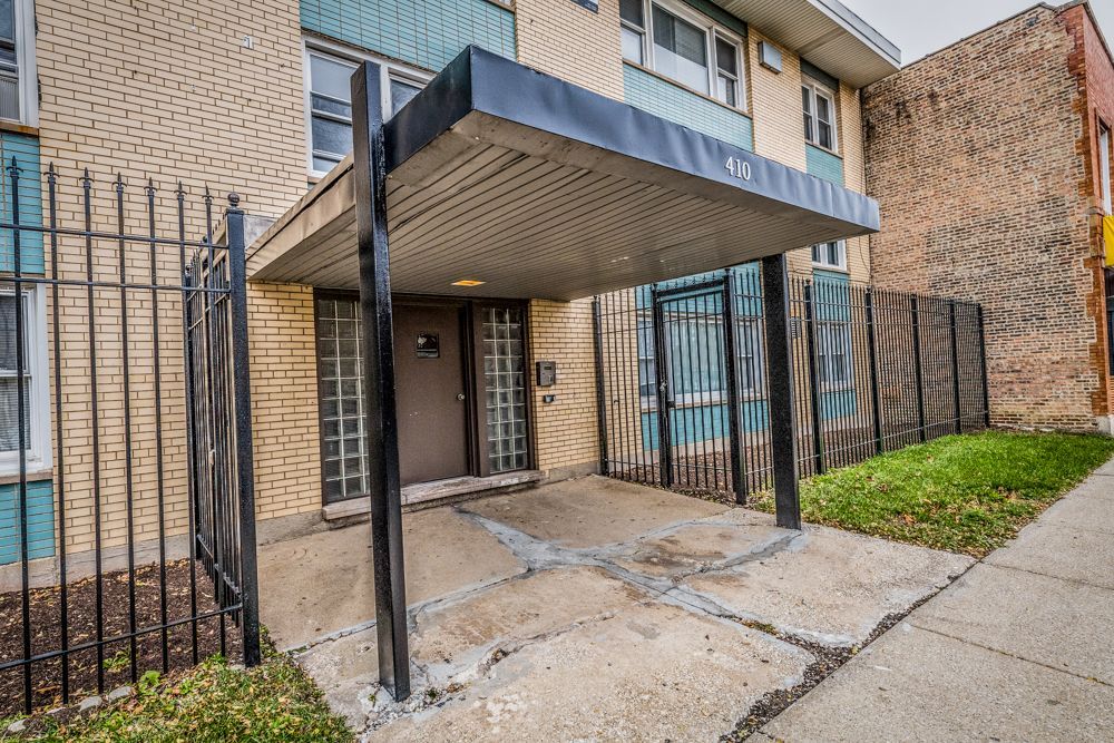 Entrance to a multi-unit building with a black awning, metal gate, and concrete walkway.