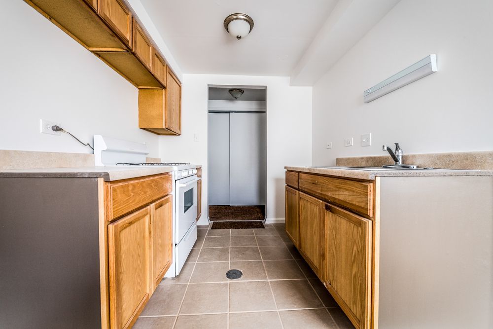 Empty kitchen with light wood cabinets, white appliances, and tiled floor.