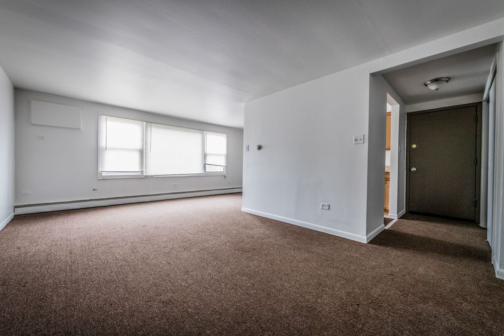 Empty living room with brown carpet, white walls, and a doorway.
